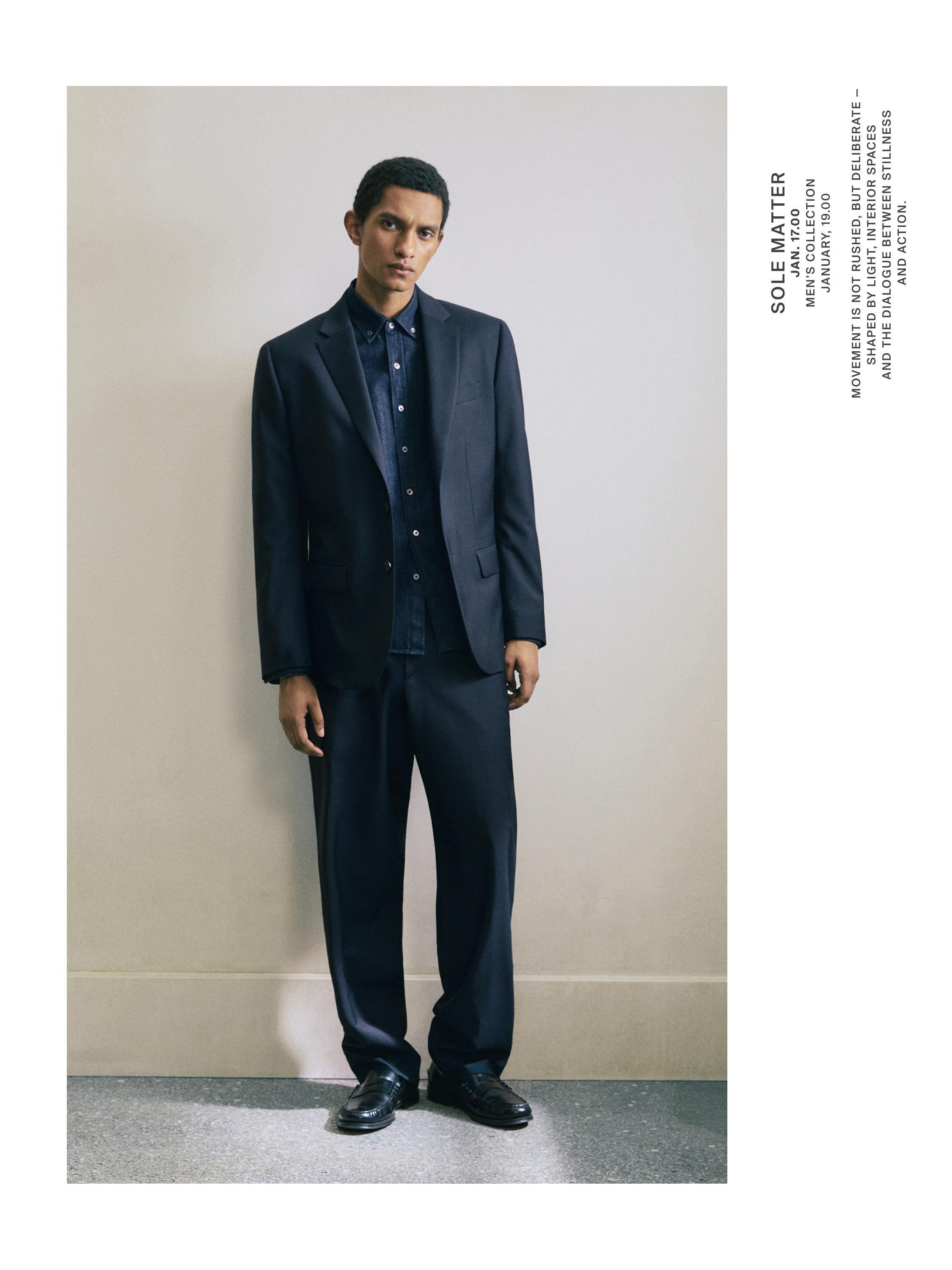 طقم بدلة كحلي مع سترة بزرين، قميص أزرق وبنطلون بقصة مستقيمة.