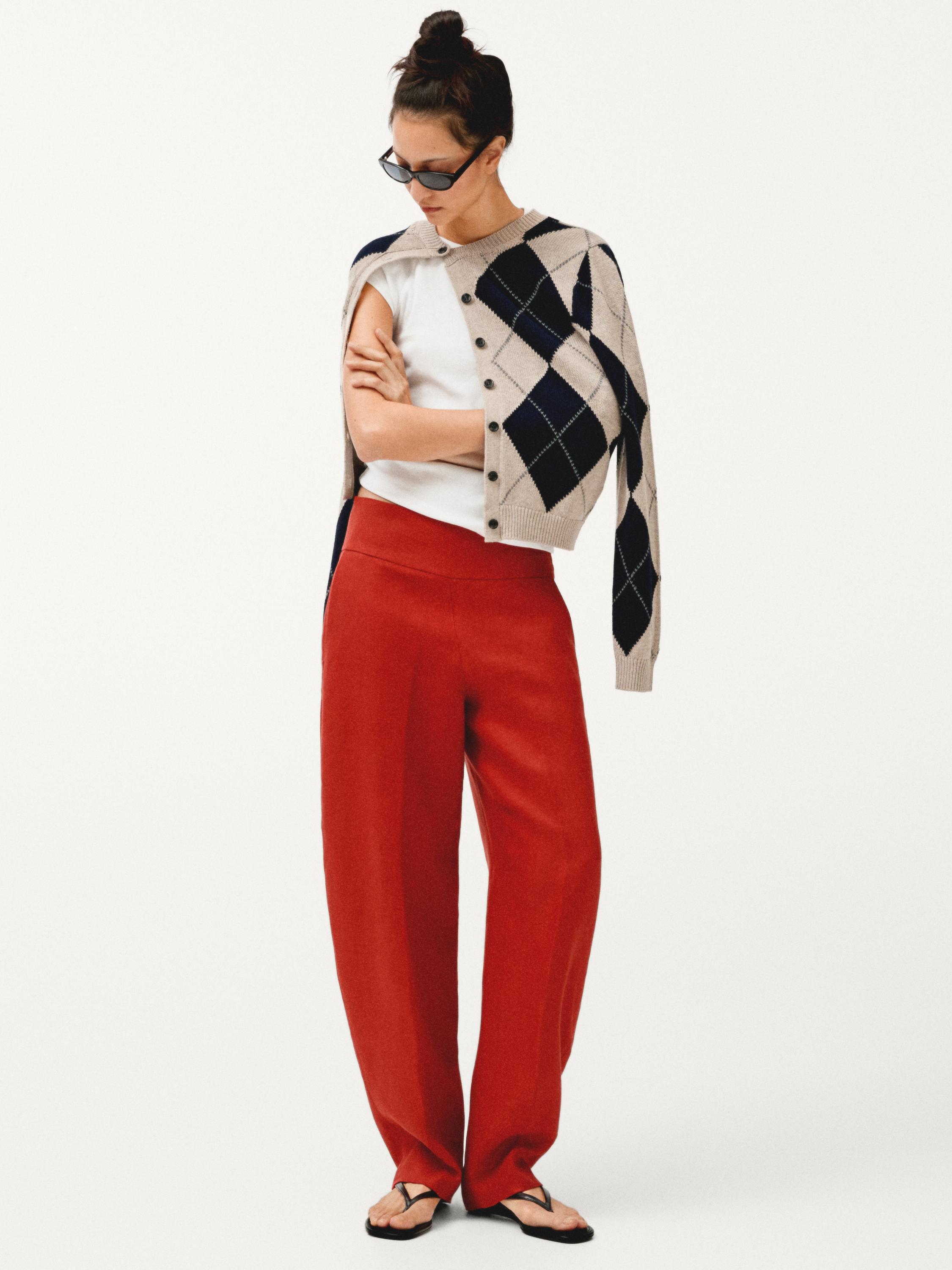 넉넉한 핏의 빨간색 바지, 흰색 티셔츠, 그리고 어깨에 파란색 마름모 무늬가 있는 베이지색 카디건 세트.