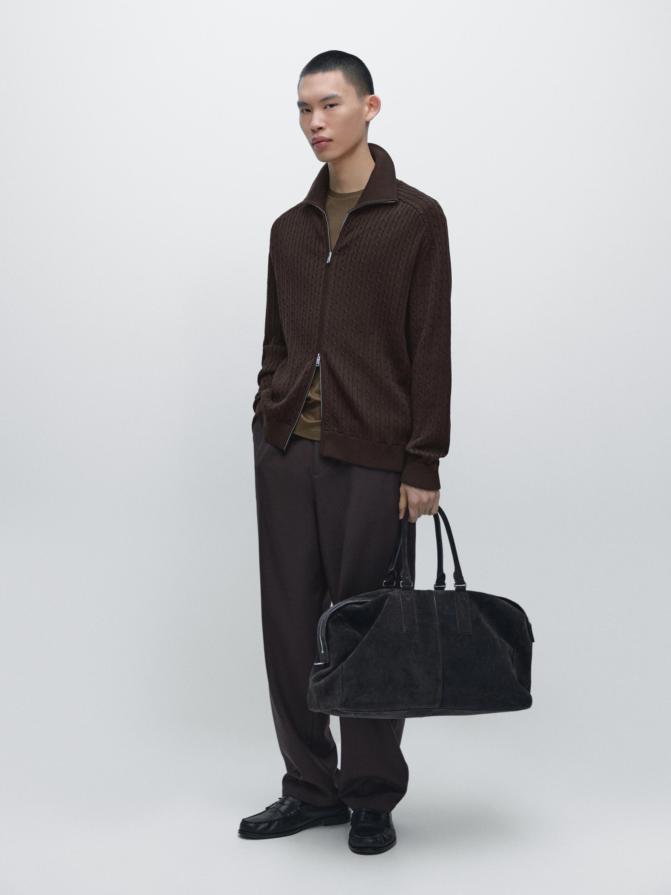 Mêle bruin vest met rits en kabelsteek, donkere broek en zwarte handtas.