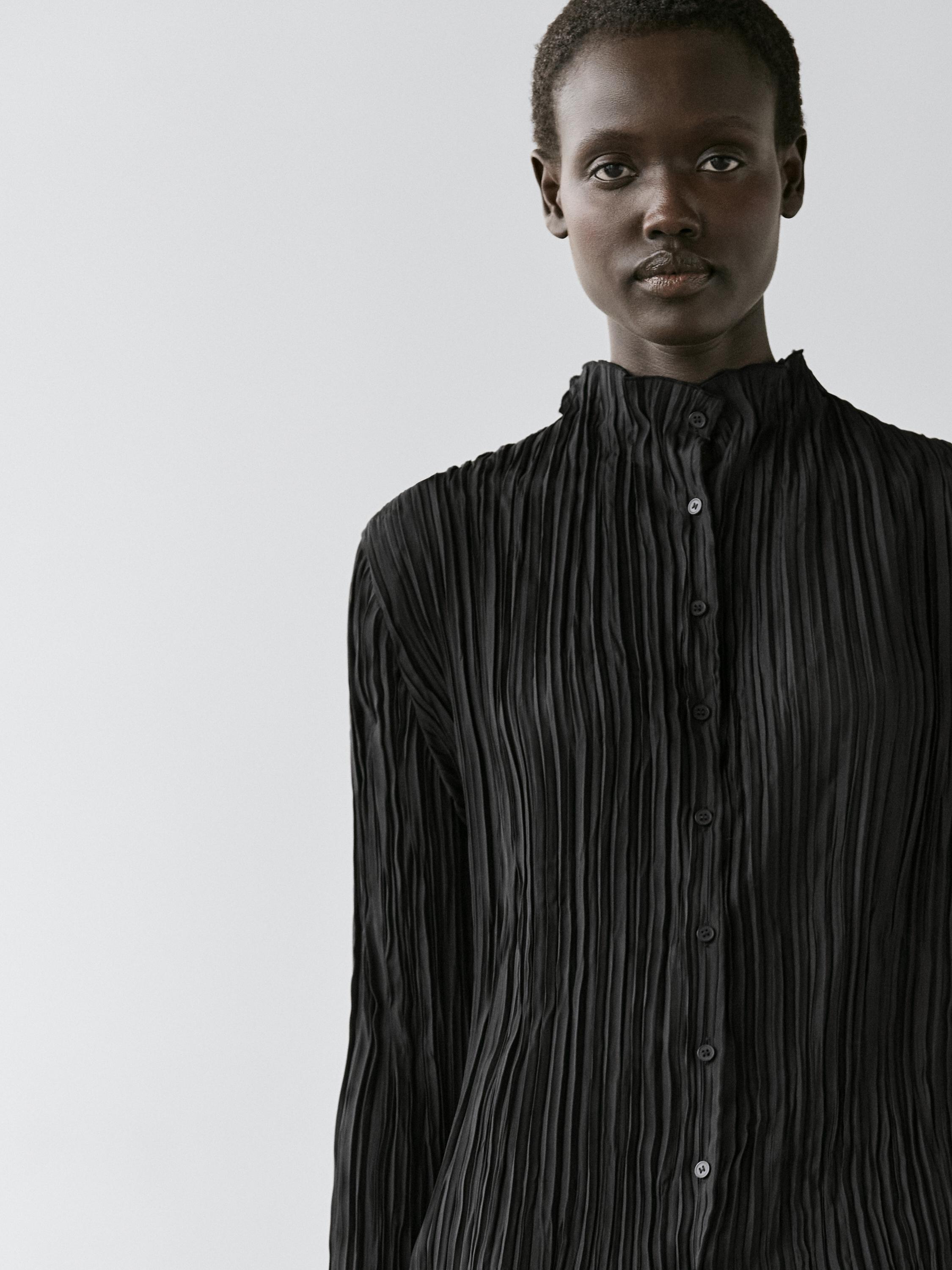 Plan moyen d'une chemise noire fluide avec détail plissé et boutonnage frontal.