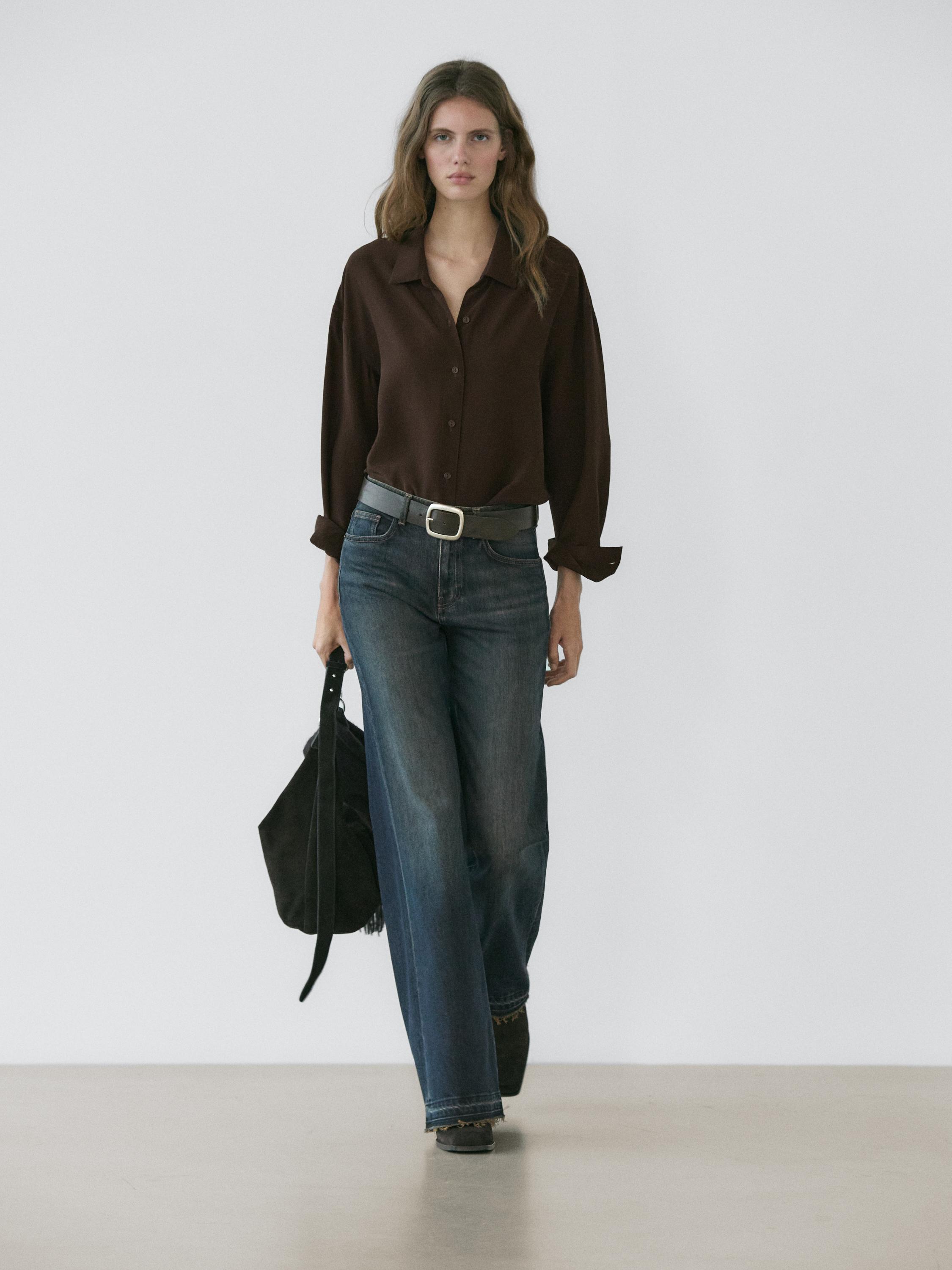Ensemble chemise marron boutonnée et jean large bleu foncé. Ceinture noire avec boucle argentée visible.