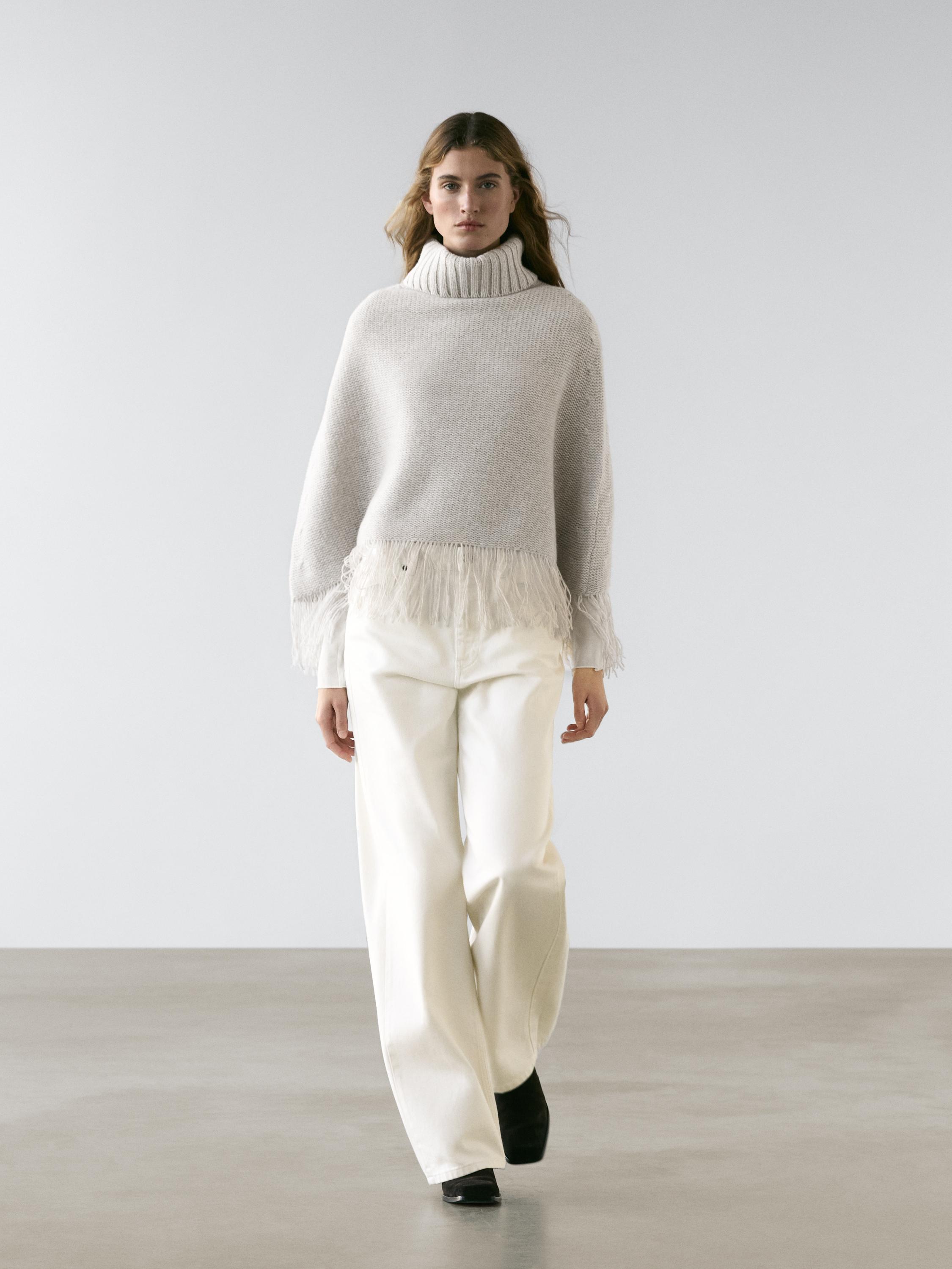 Anthracite gray turtleneck sweater set with fringe on the hem, wide white pants, and black shoes.