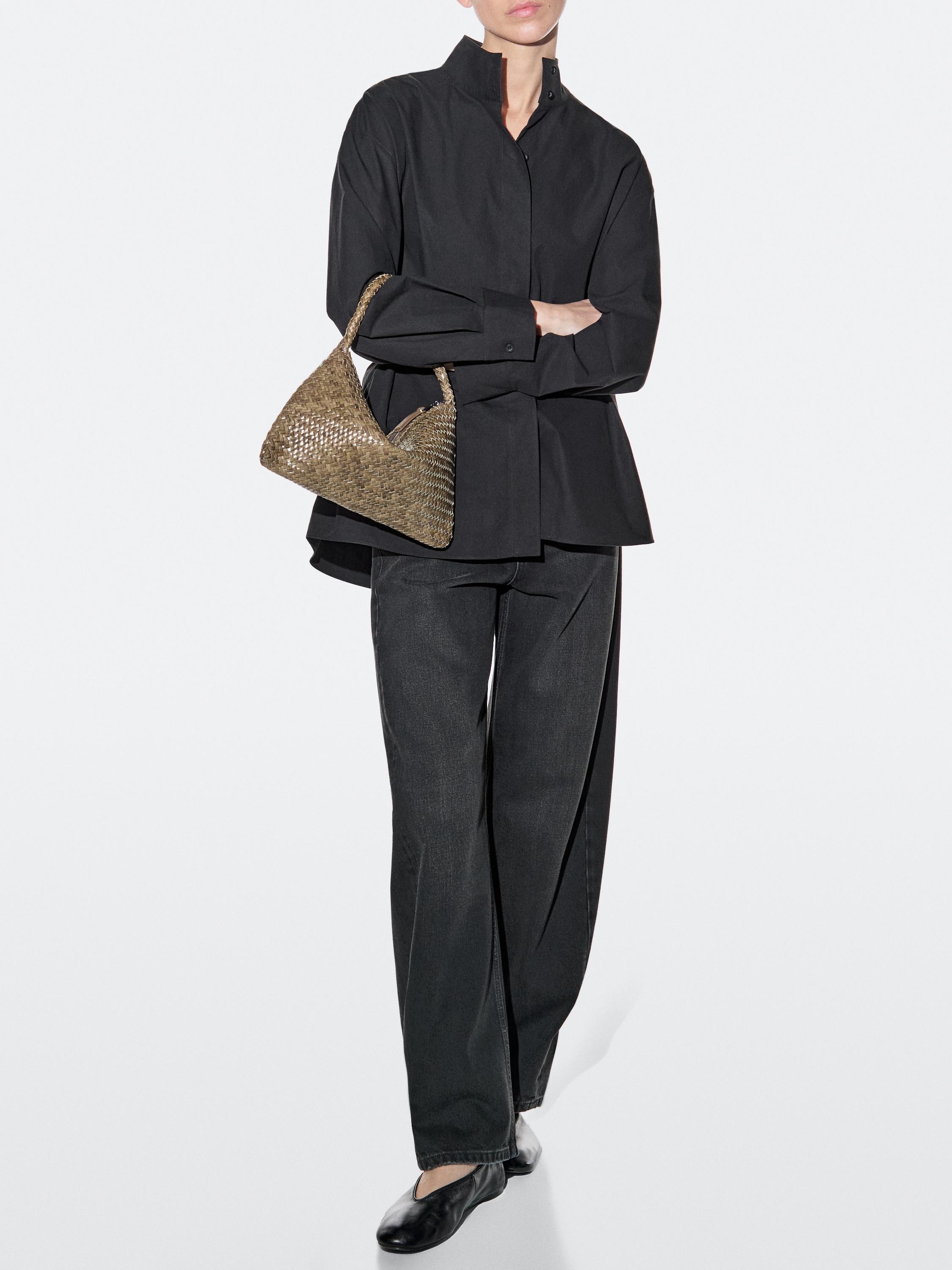 Conjunto de camisa negra de manga larga, pantalones anchos negros y bolso de mano kaki tejido.