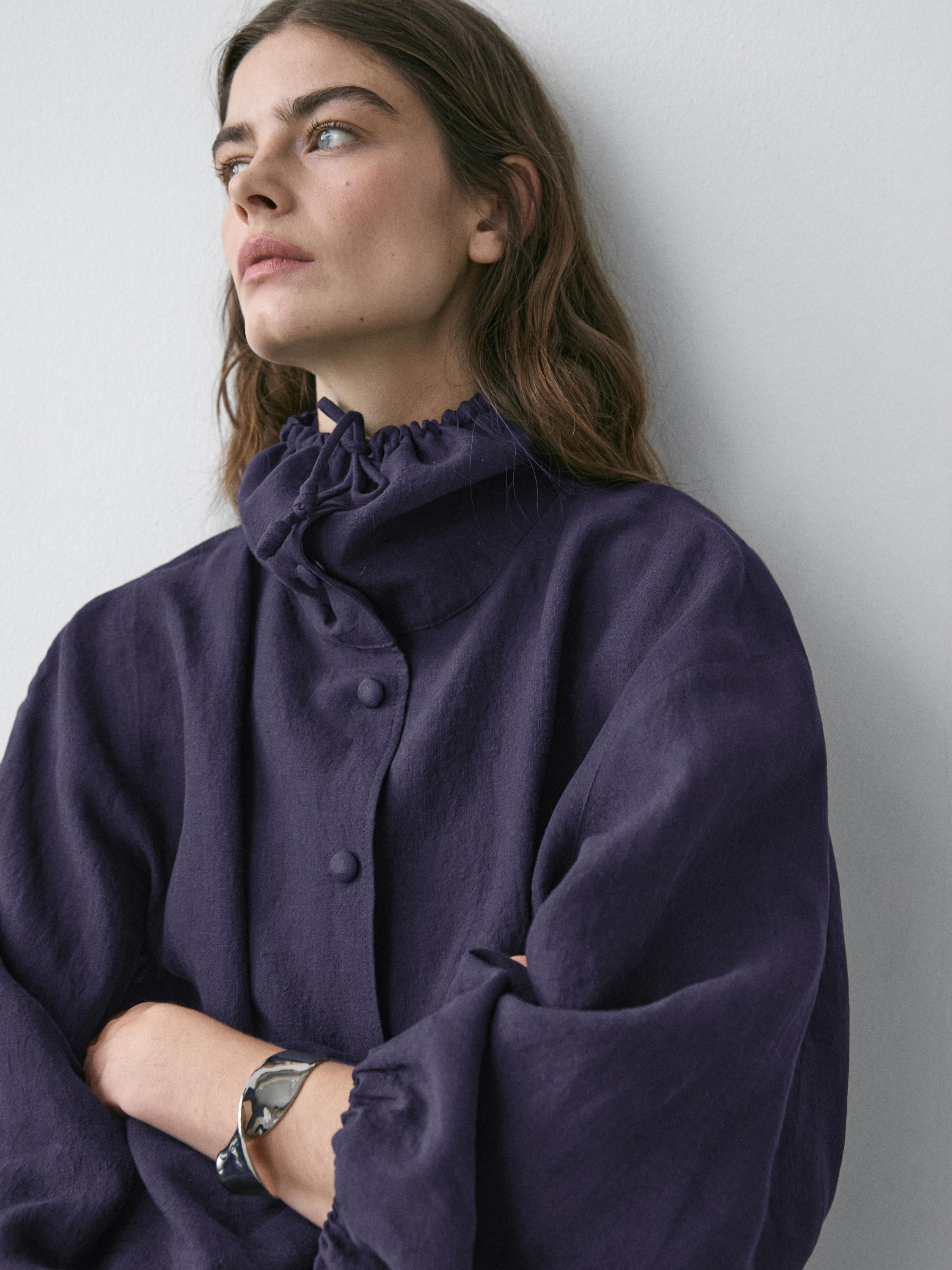 İndigo bomber ceketin büzgülü yakalı ve kapalı düğmeli orta çekimi.