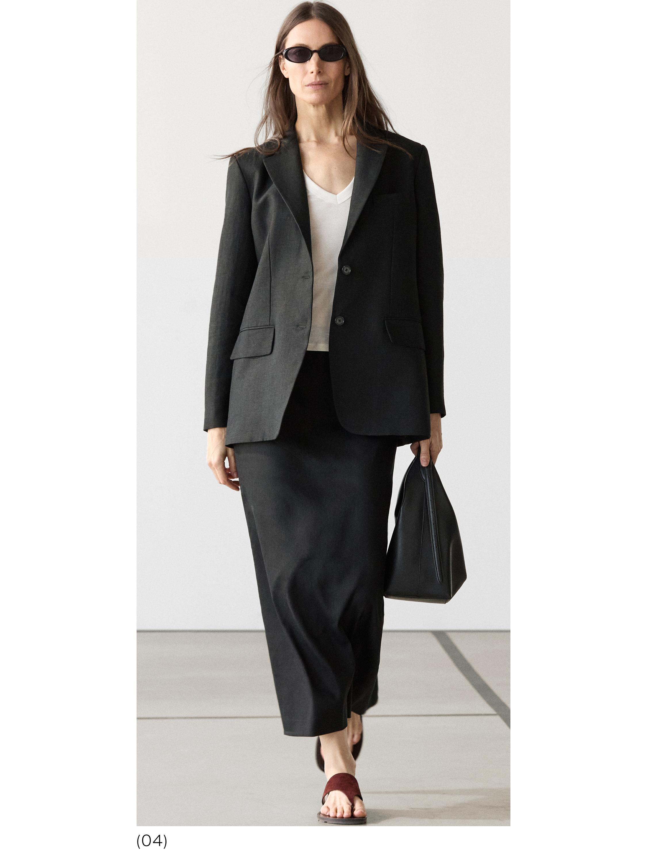 Conjunto de blazer negro con bolsillos y falda larga negra, camiseta blanca y sandalias marrones.