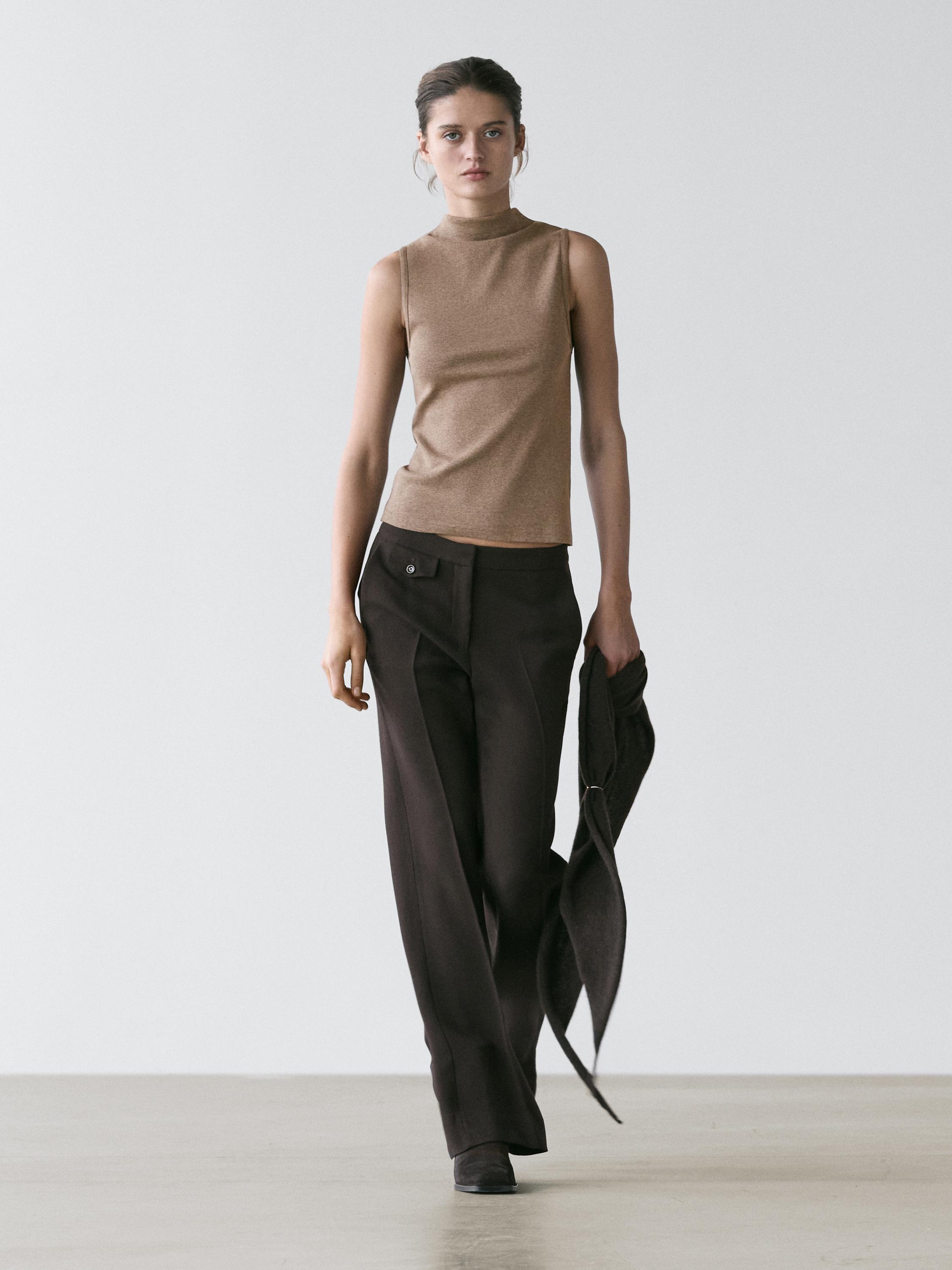 Conjunto de top sin mangas visón con cuello chimenea y pantalones oscuros de pierna ancha con bolsillo lateral.