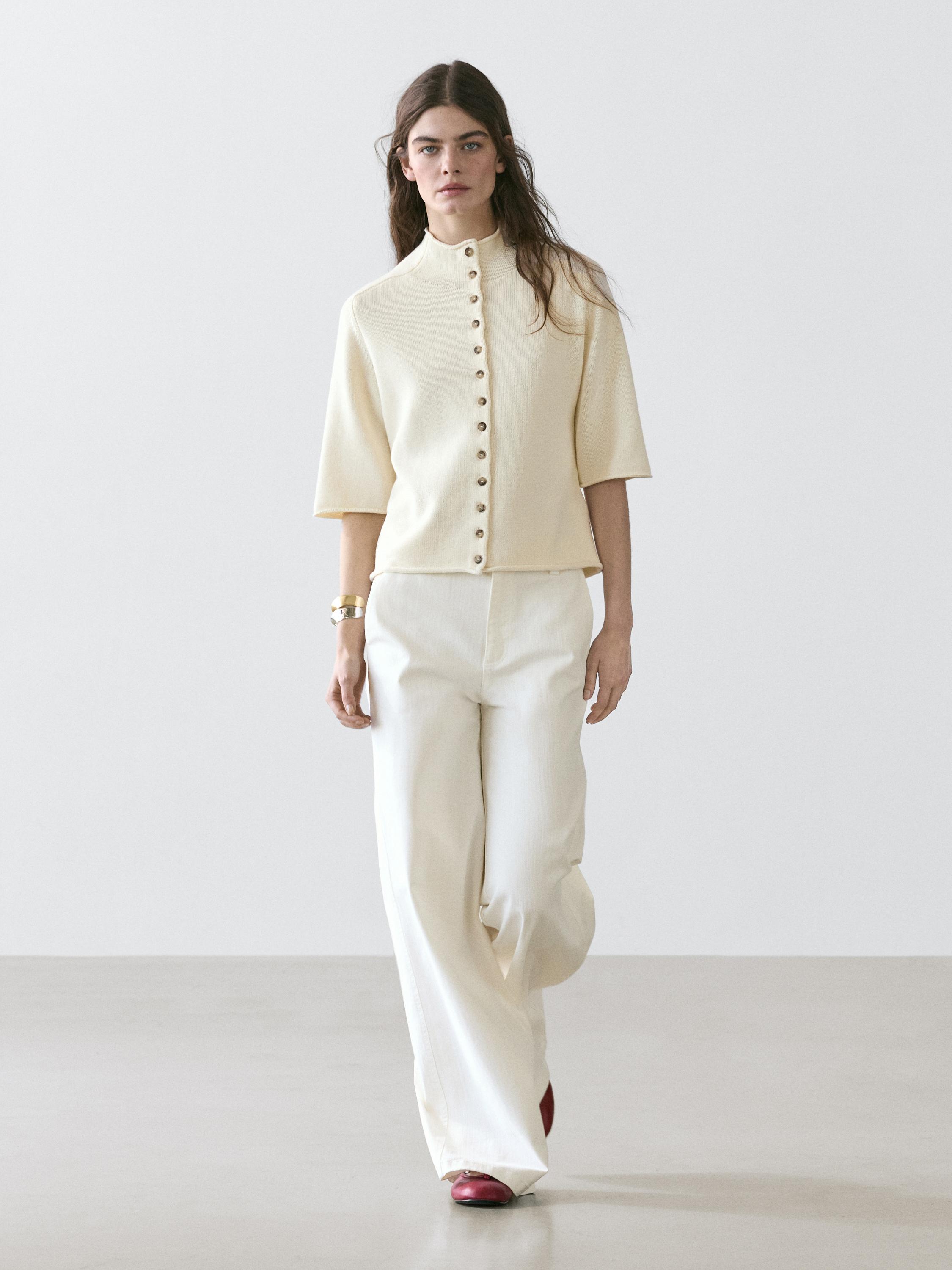 Set aus beiger Bluse mit Knöpfen und kurzen Ärmeln, weißen High-Waist-Palazzo-Hosen und roten Schuhen.