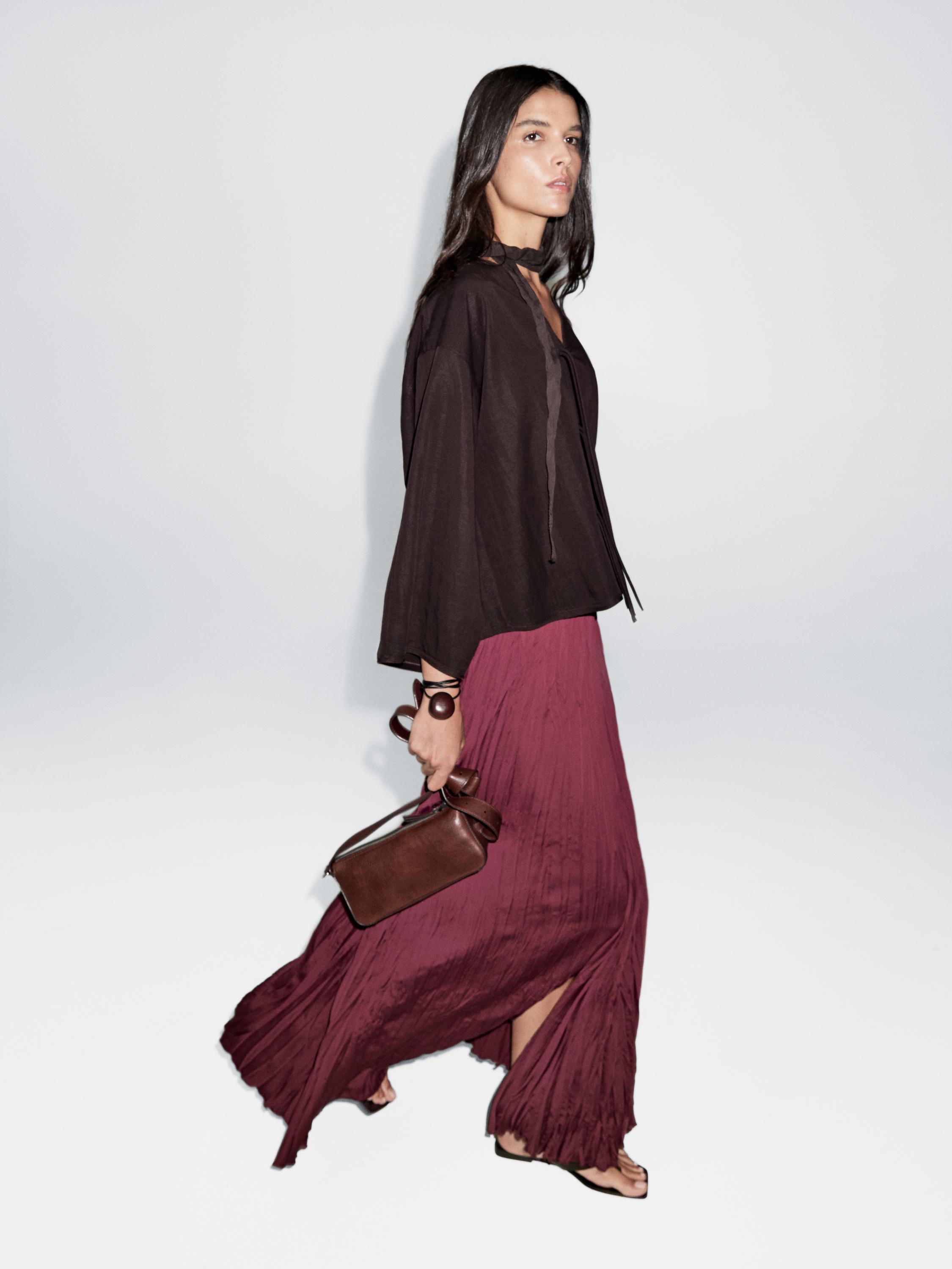 Outfit of loose brown blouse and long pleated burgundy skirt, with brown bag and flat sandals.
