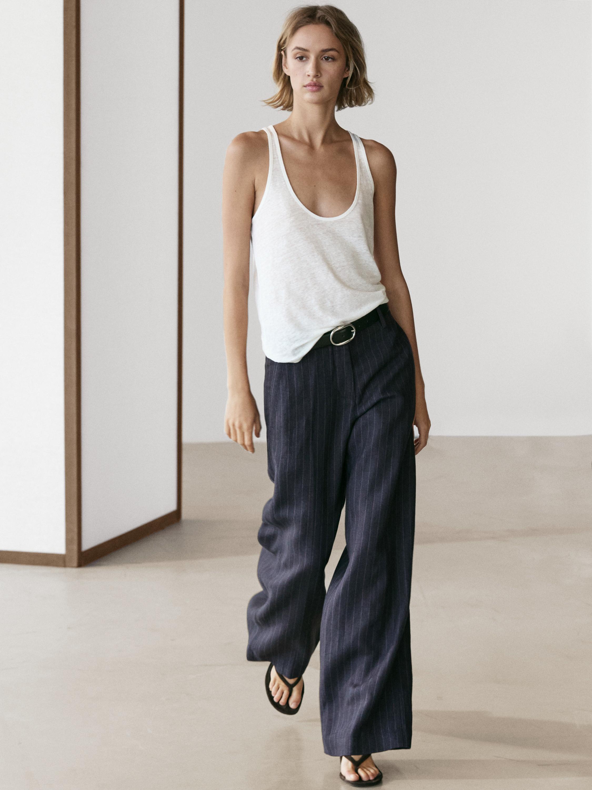 Donkerblauwe wide-leg broek met krijtstreep en witte mouwloze top.
