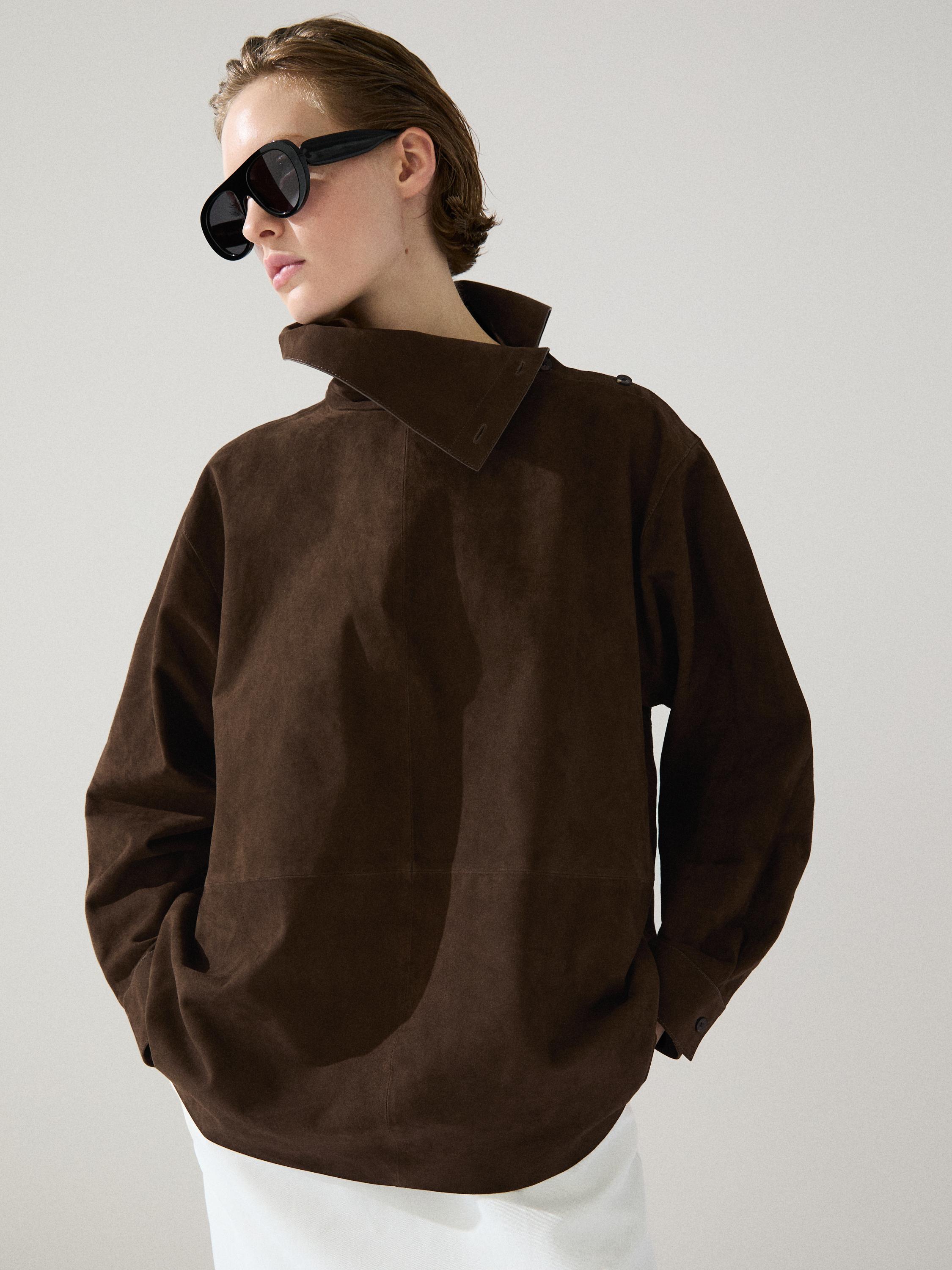 Zbliżenie na brązową bluzkę z wysokim kołnierzem i bocznymi kieszeniami.