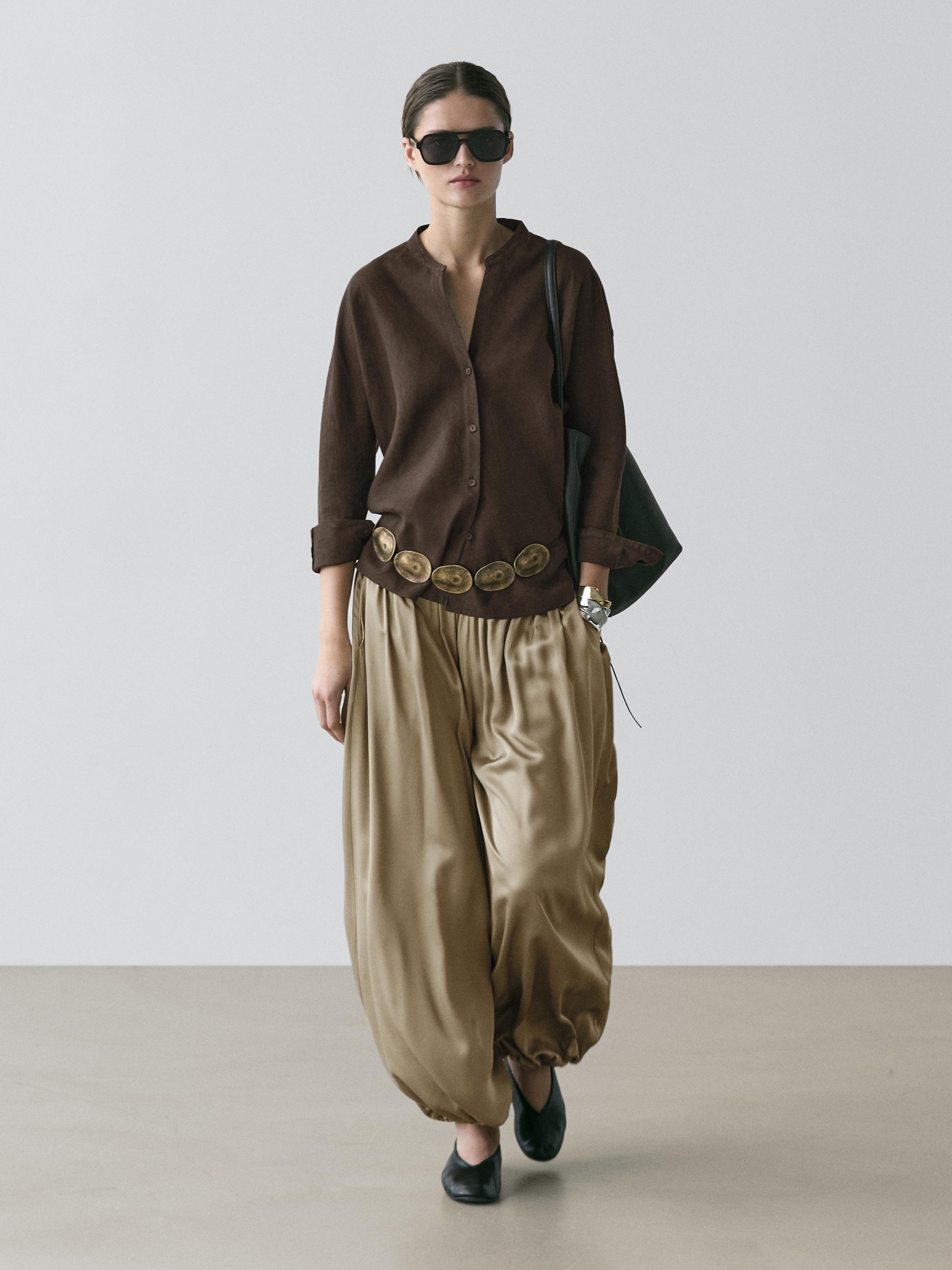 Conjunto de camisa marrón de cuello mao y pantalones anchos beige con cinturón decorativo y zapatos negros.