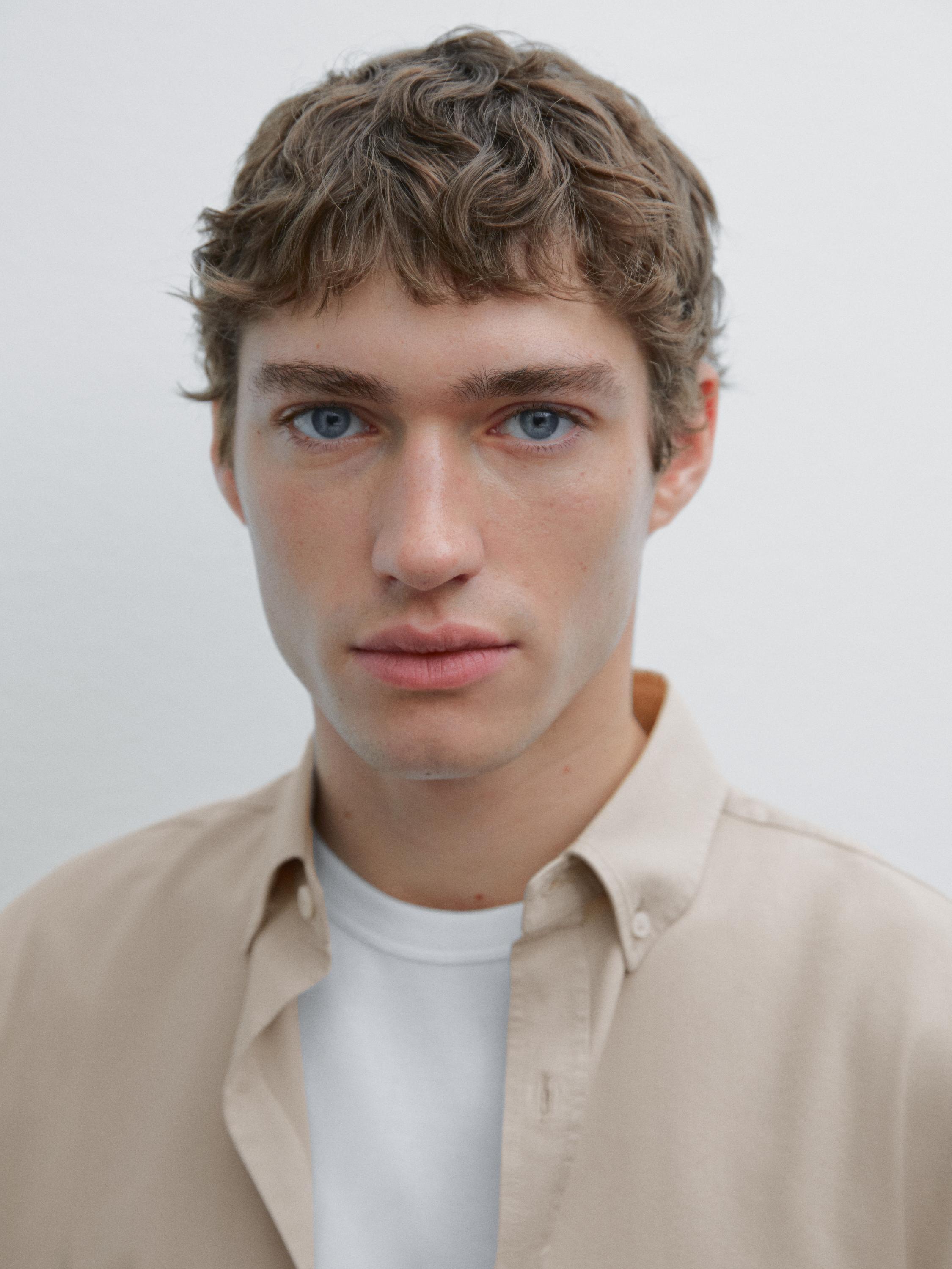 Plan moyen d'une chemise beige déboutonnée sur un t-shirt blanc.