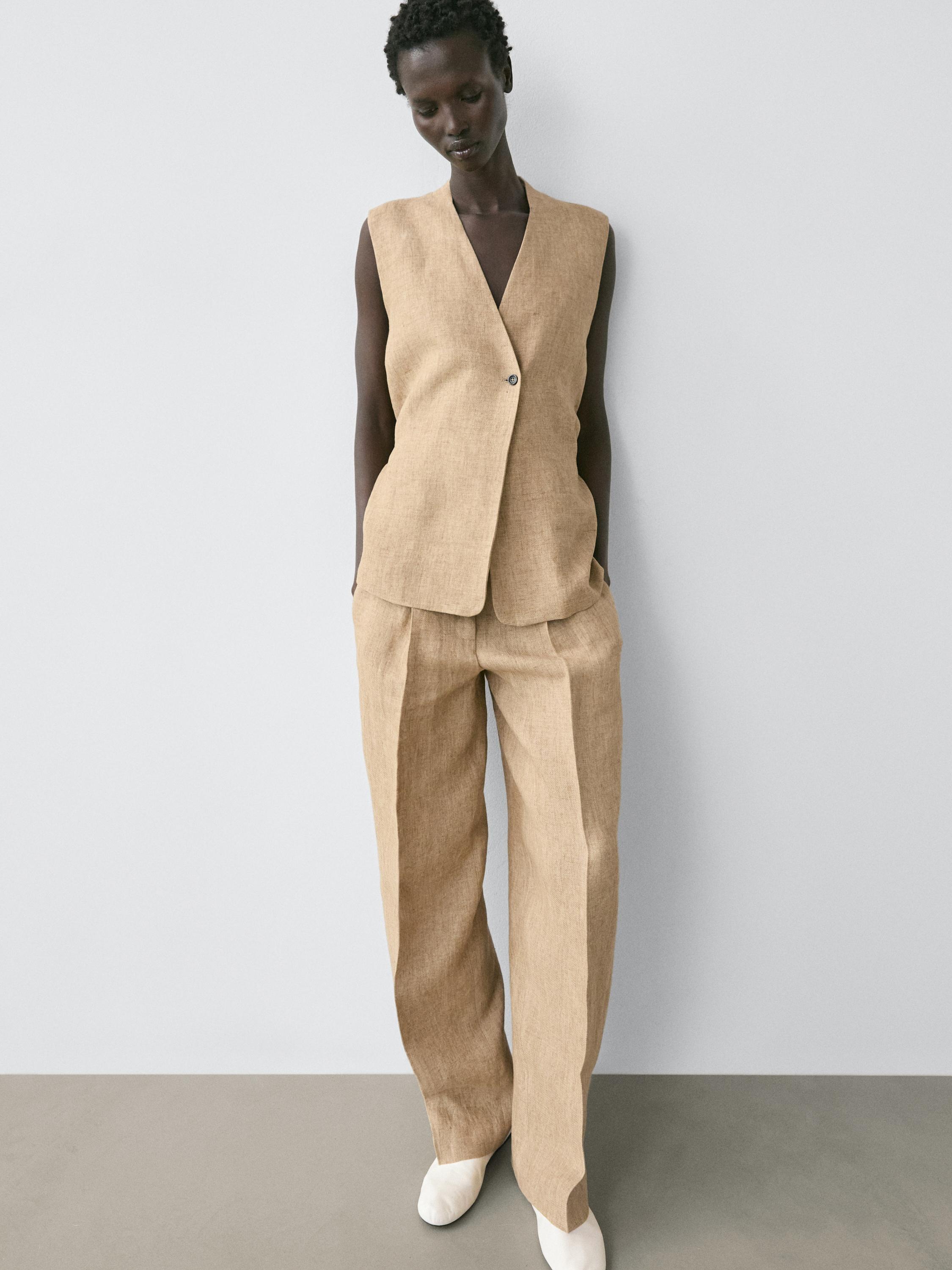 Conjunto de chaleco beige sin mangas con cierre cruzado y pantalones anchos a juego, bolsillos laterales visibles.