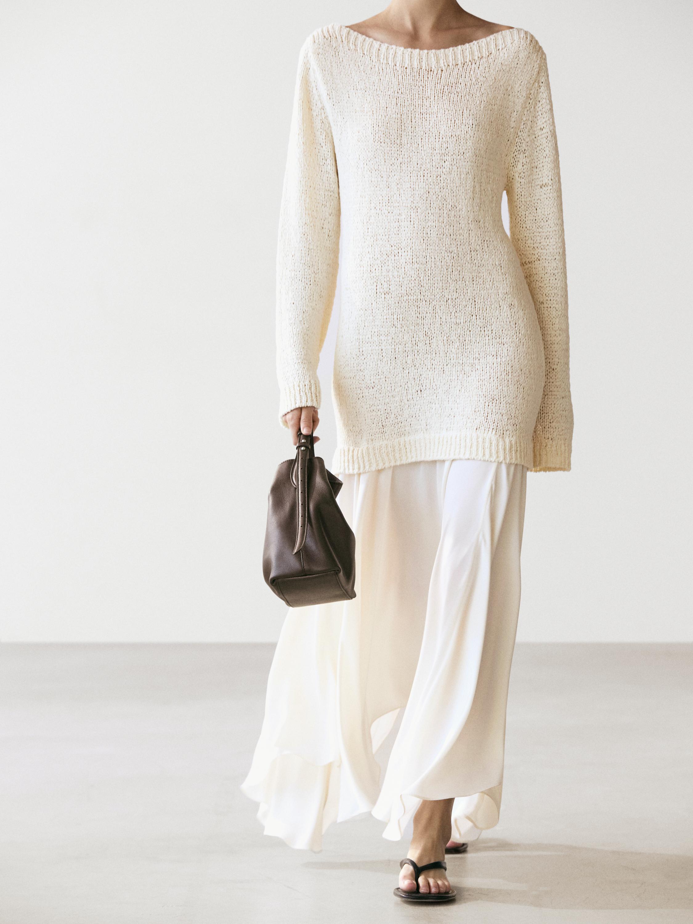 Conxunto de vestido midi cru asimétrico con xersei longo de punto cru, bolso marrón e sandalias negras.