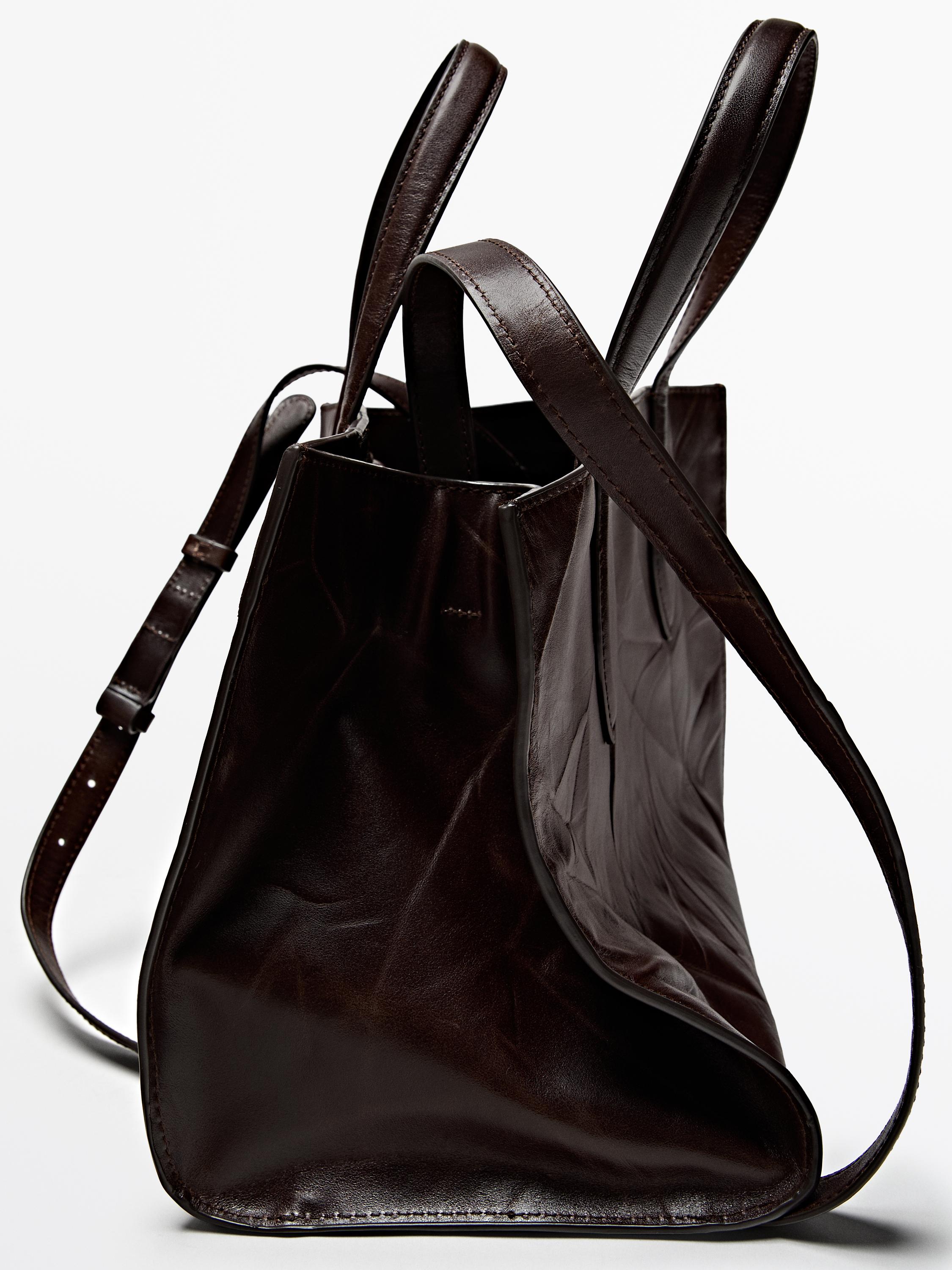 Vista lateral de bolsa marrón con asas dobres e correa axustable. Dimensións: 20 x 28 x 17 cm.