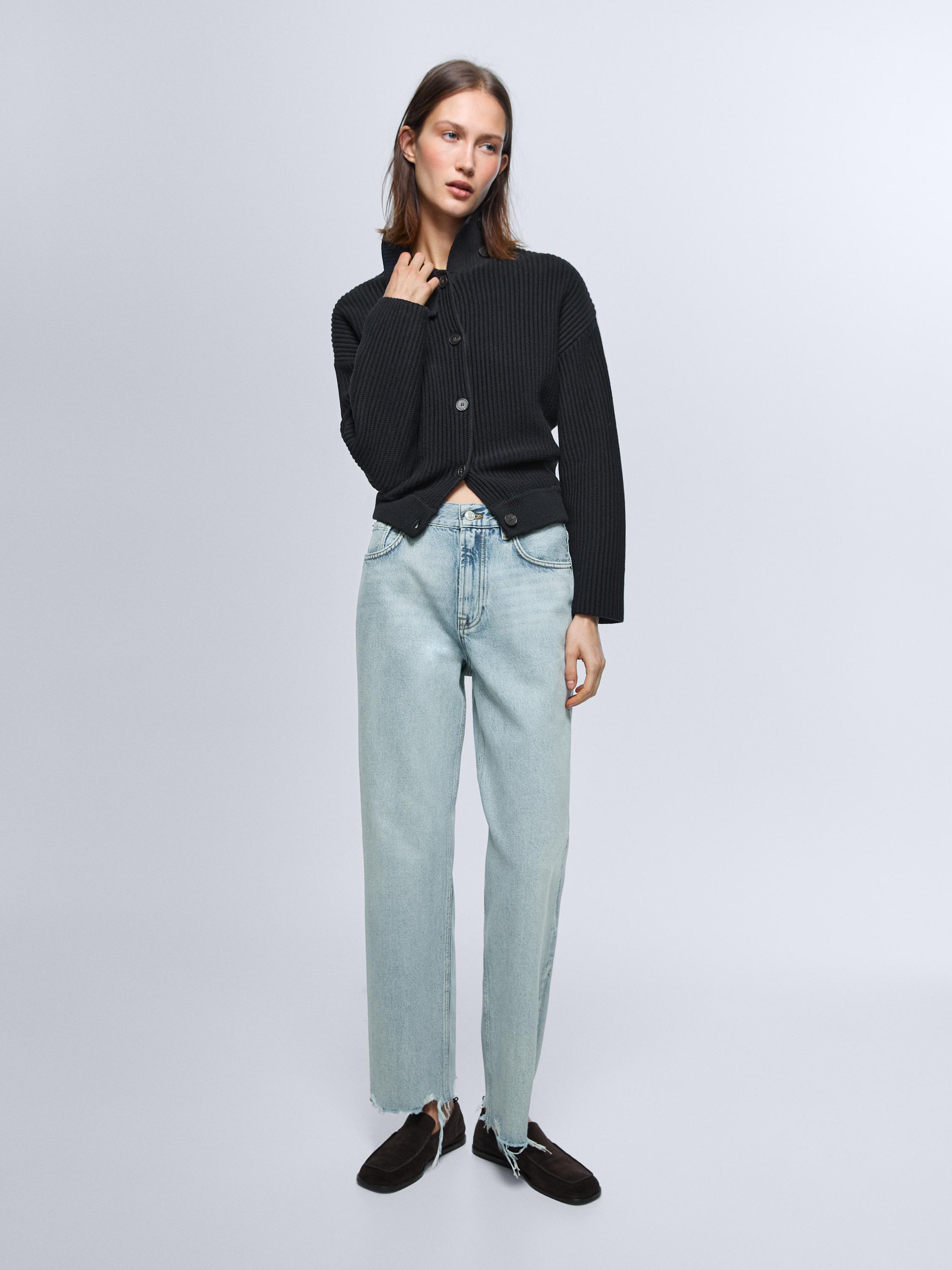 Zestaw: czarny, dzianinowy kardigan zapinany na guziki oraz jasnoniebieskie, proste jeansy z wysokim stanem i postrzępionymi nogawkami.
