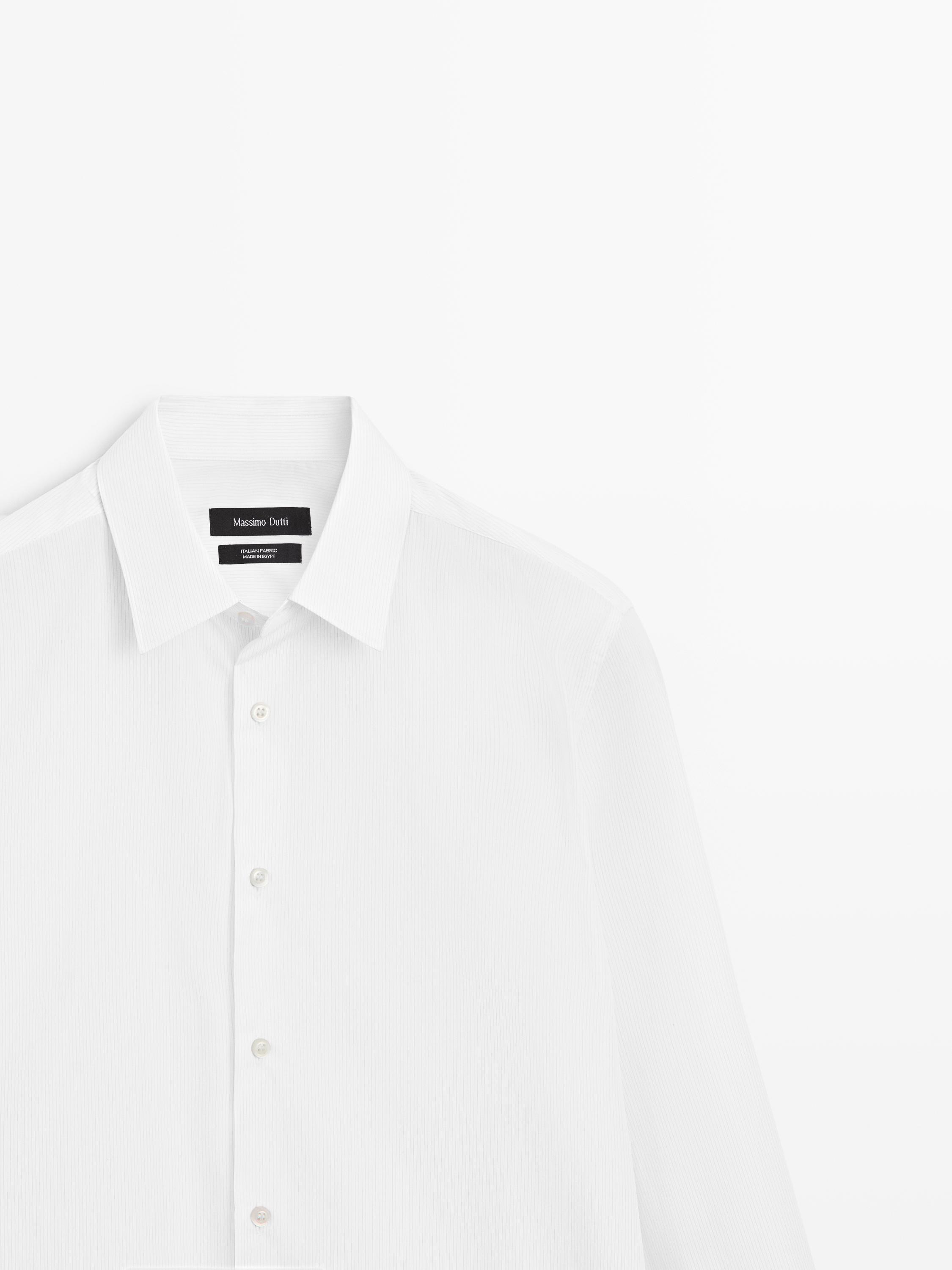 "Plano medio de camisa blanca de manga larga con cuello clásico y botonadura frontal."