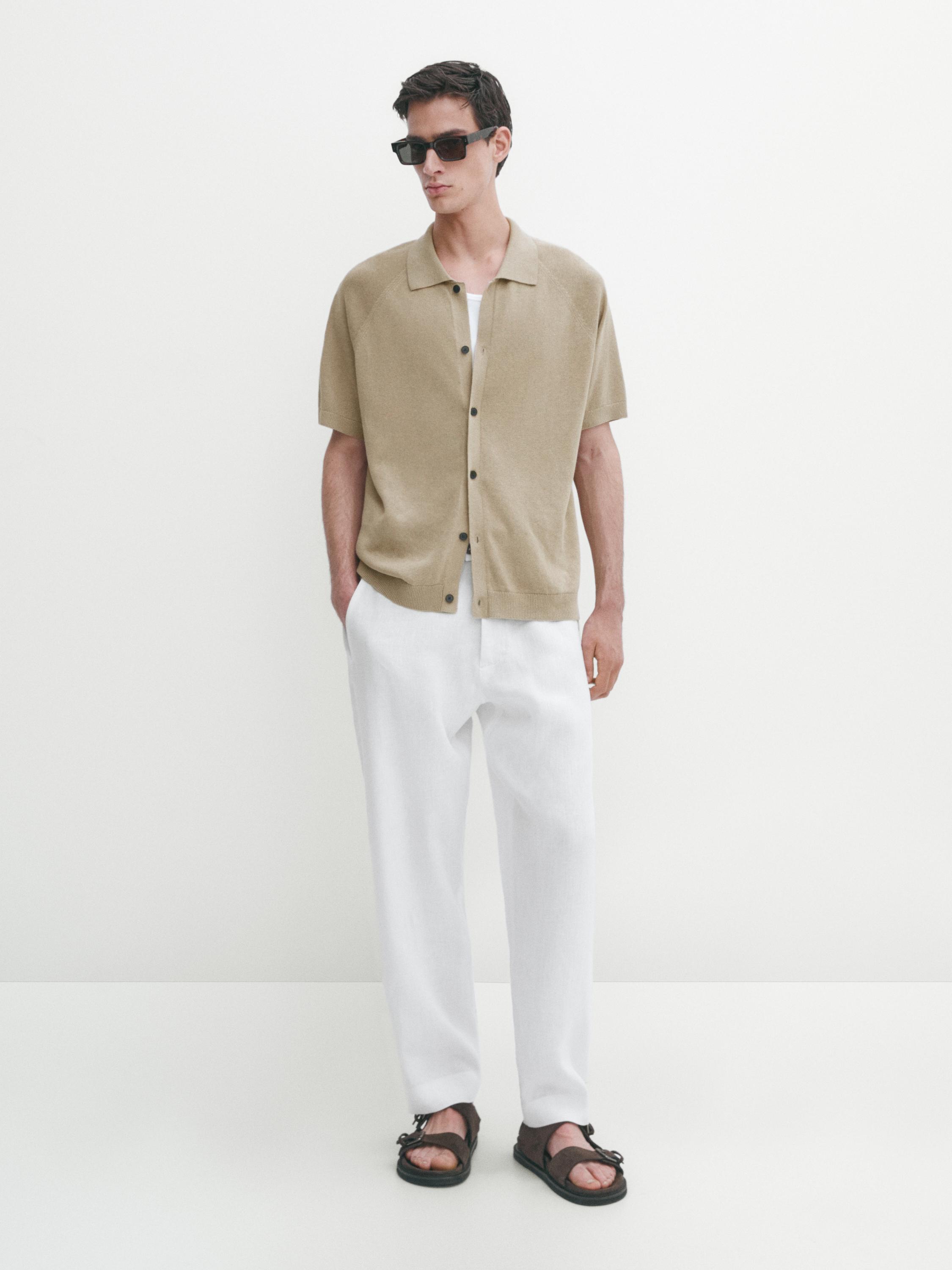 Ensemble composé d'une chemise beige à manches courtes boutonnée et d'un pantalon blanc.