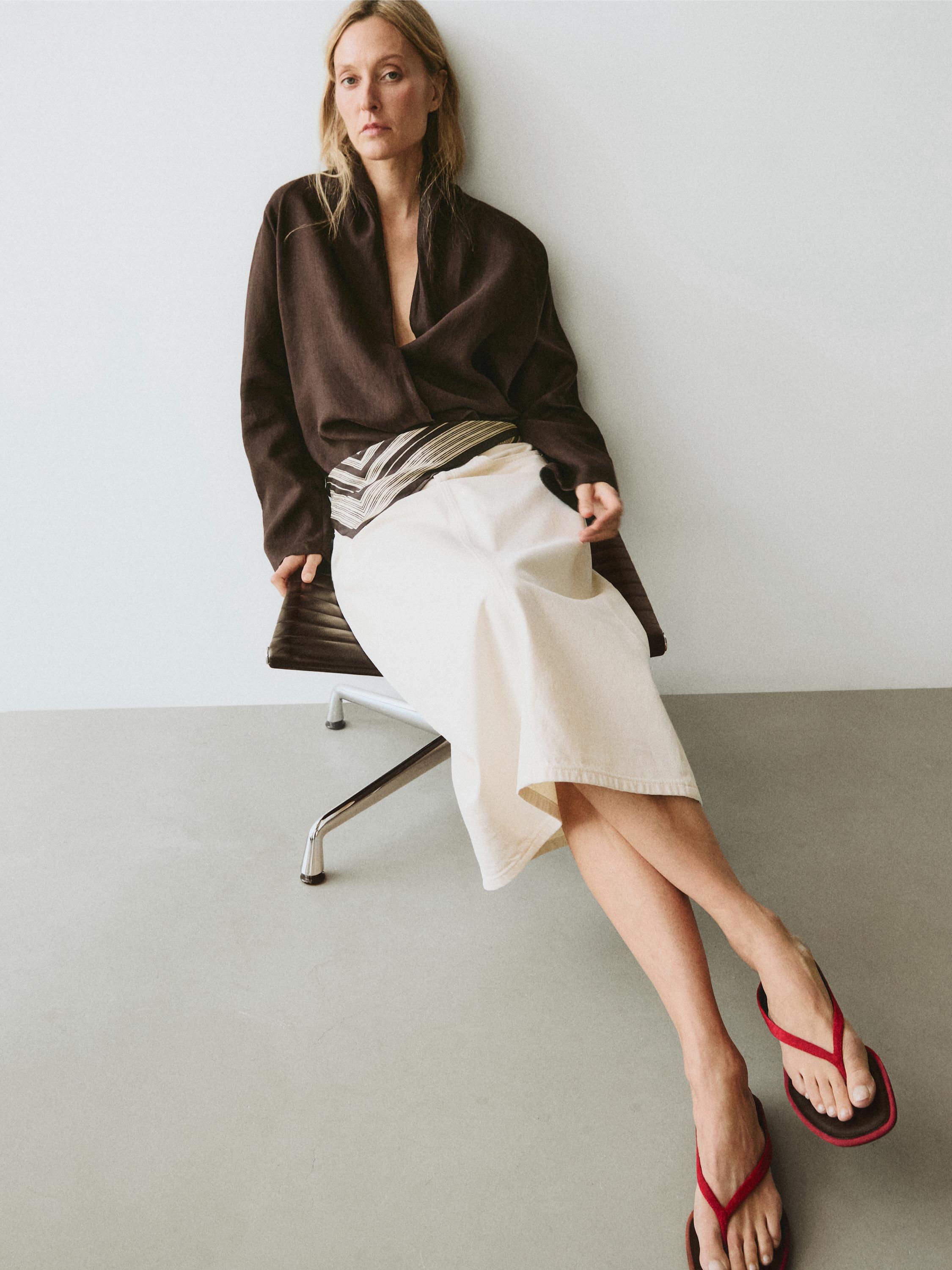 Zestaw składający się z brązowej bluzki kopertowej i długiej białej spódnicy w paski z paskiem. Widoczne czerwone sandały.