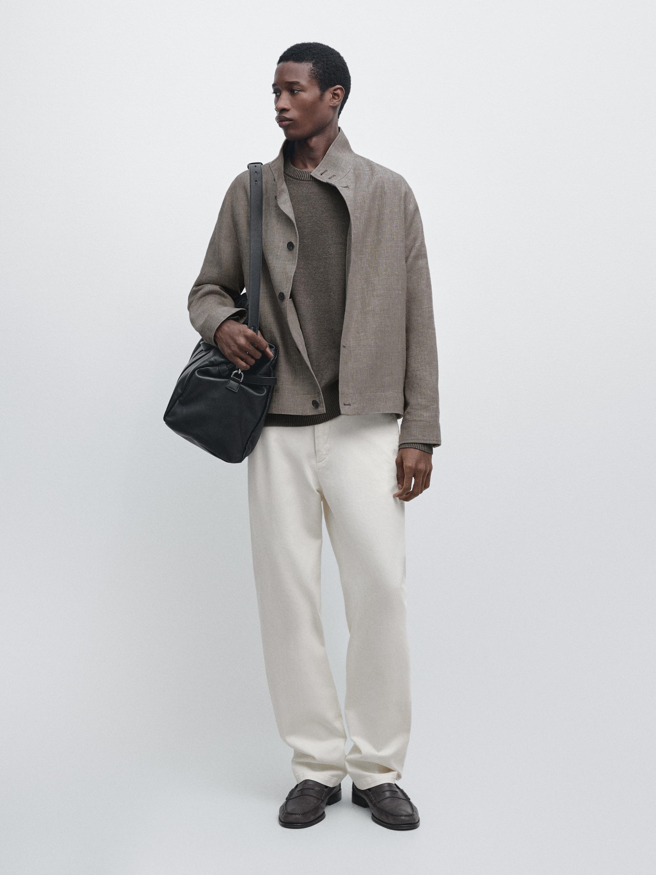 Комплект з бежевої сорочки-куртки, коричневого светра, білих штанів і коричневих туфель. Чорна сумка через плече.