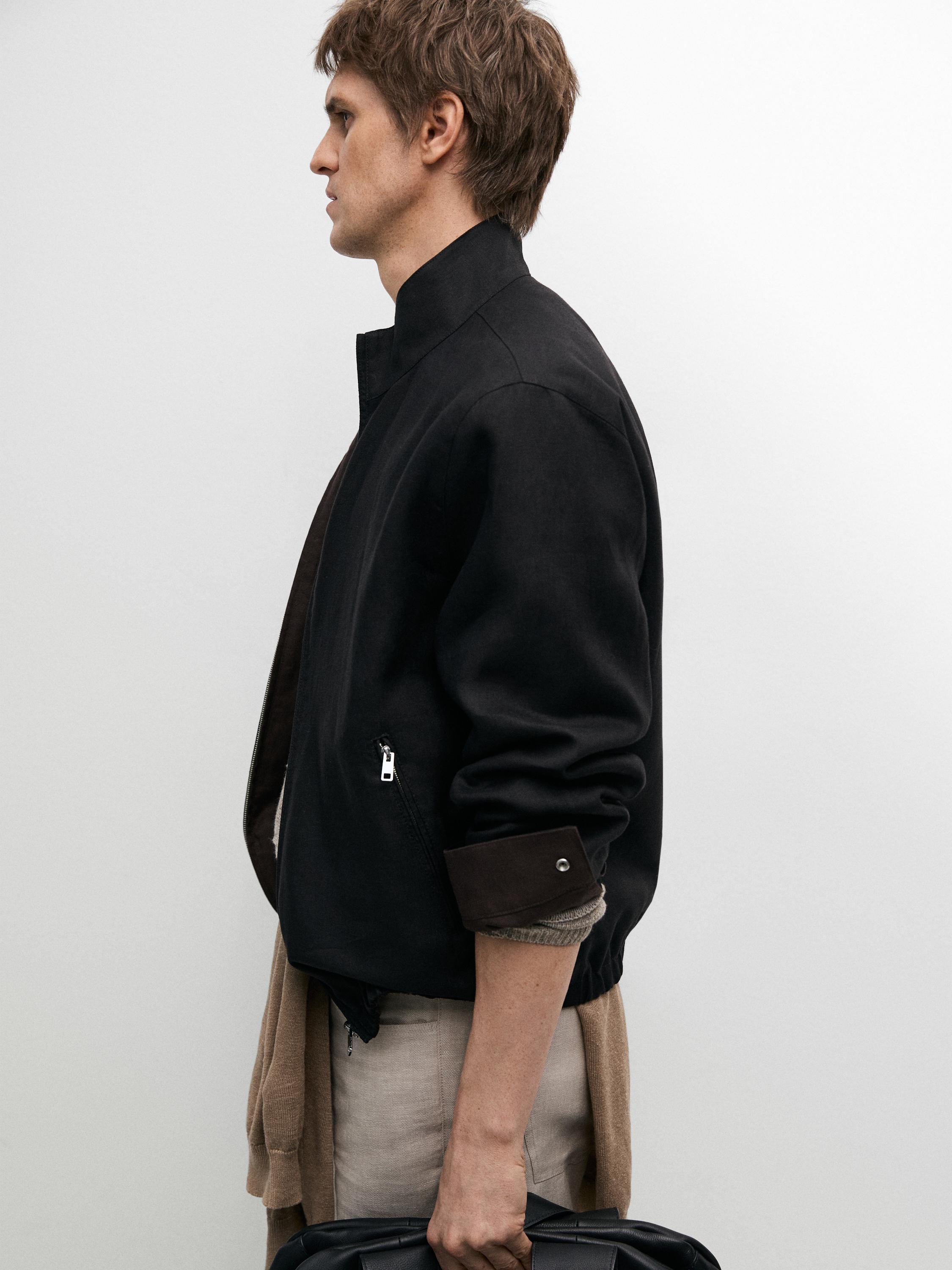 Plano medio de cazadora negra con cremallera lateral visible y puños doblados.