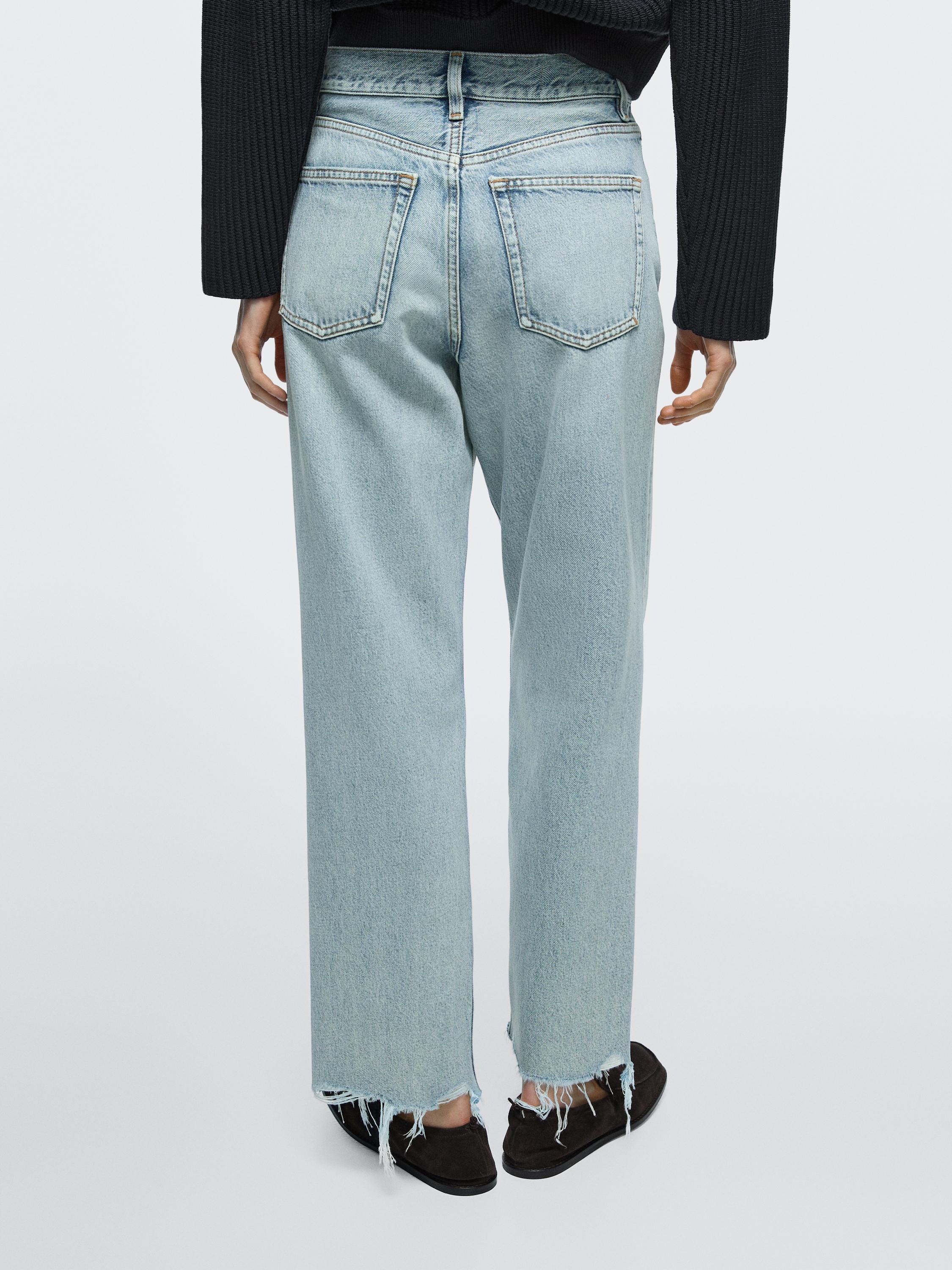 Vista posterior de *jeans* azul claro de tiro alto, corte recto, con petos traseiros e baixos desfiados.
