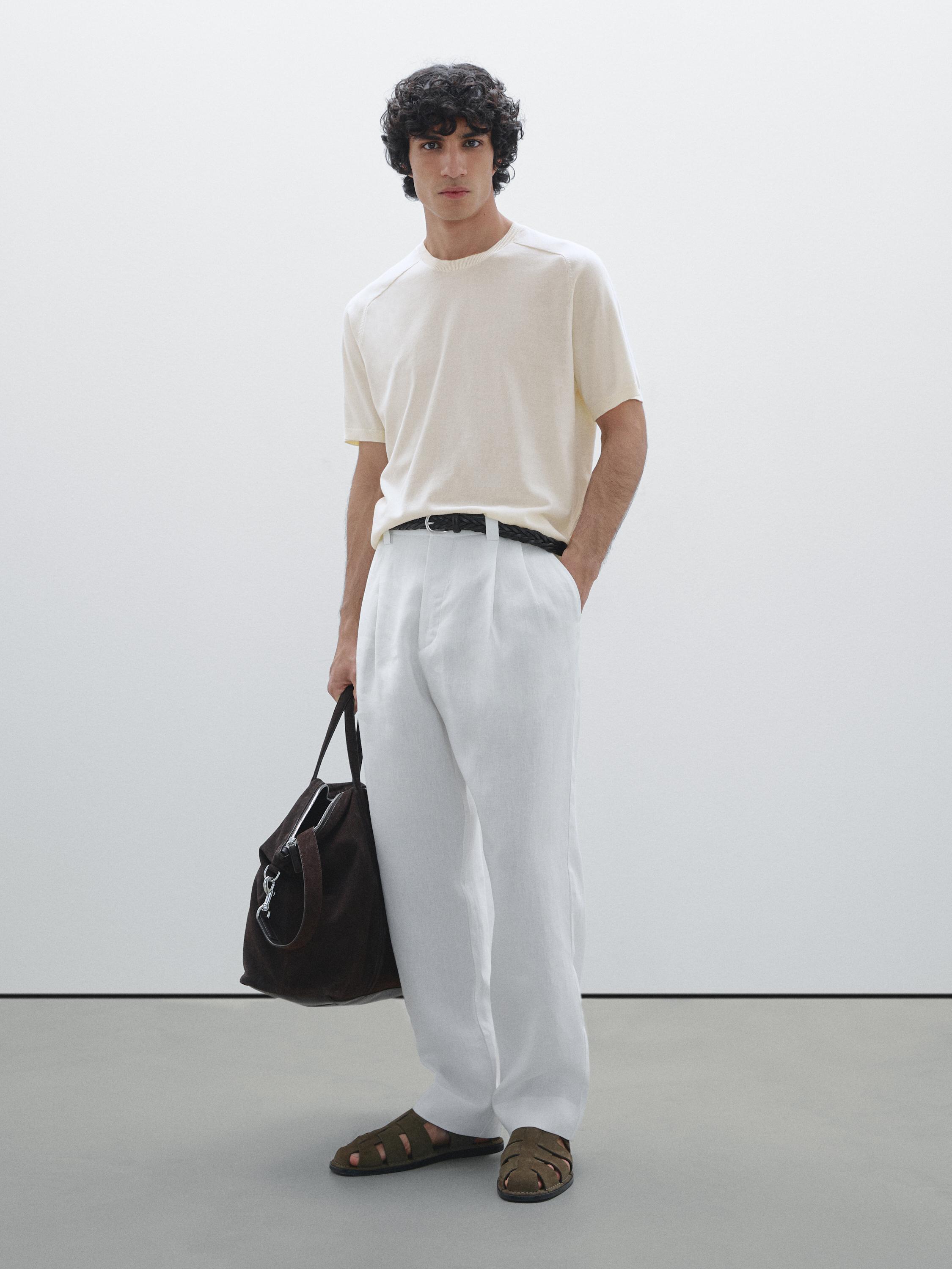 Ensemble composé d'un t-shirt beige, d'un pantalon blanc et de sandales marron, avec un sac à main foncé.