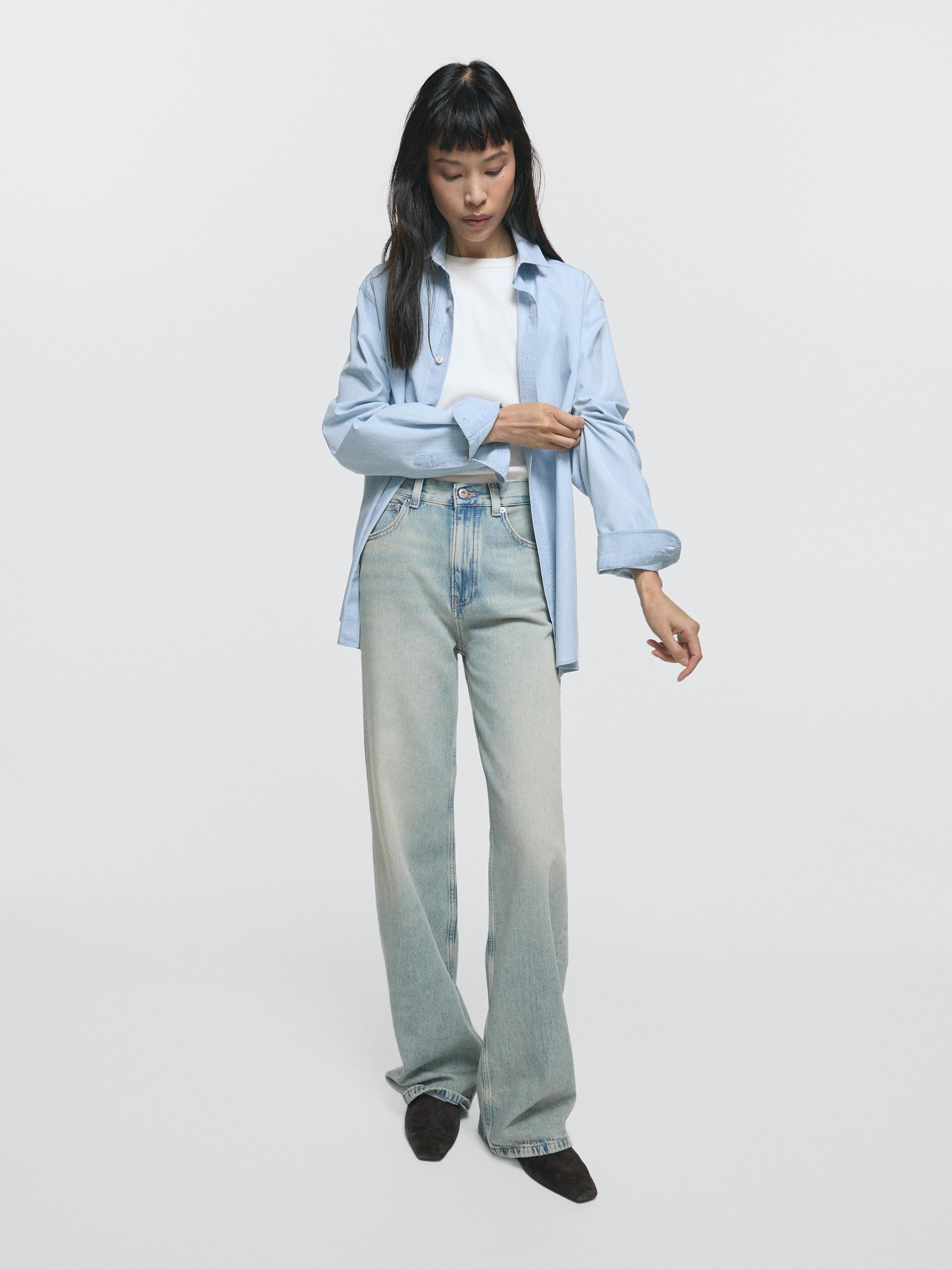 طقم مكون من قميص أزرق فاتح، تي شيرت أبيض وجينز أزرق فاتح بقصة أرجل واسعة مع جيوب أمامية.