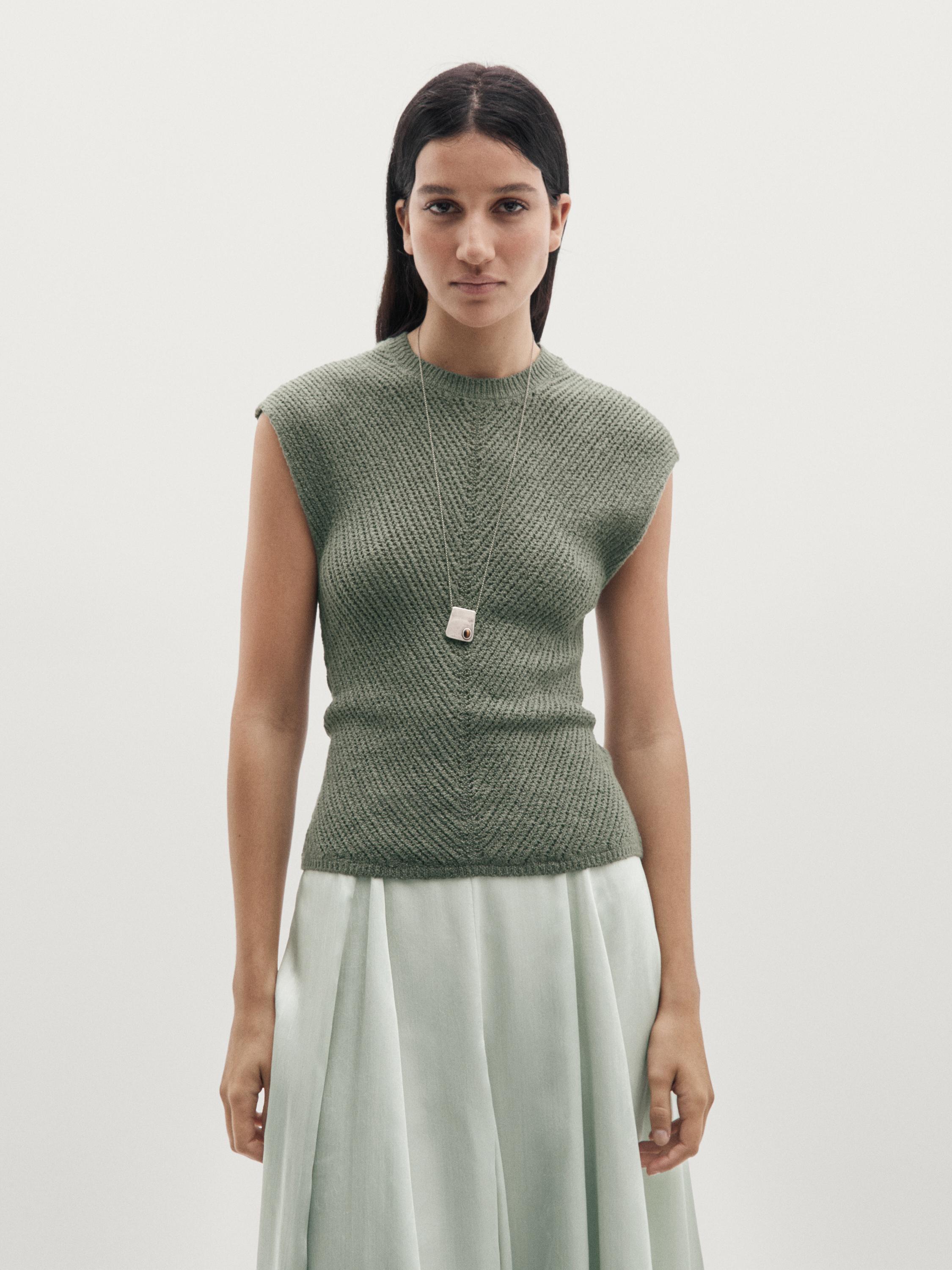 Conjunto de top verde azul sin mangas con detalles calados y falda larga plisada en tono claro.