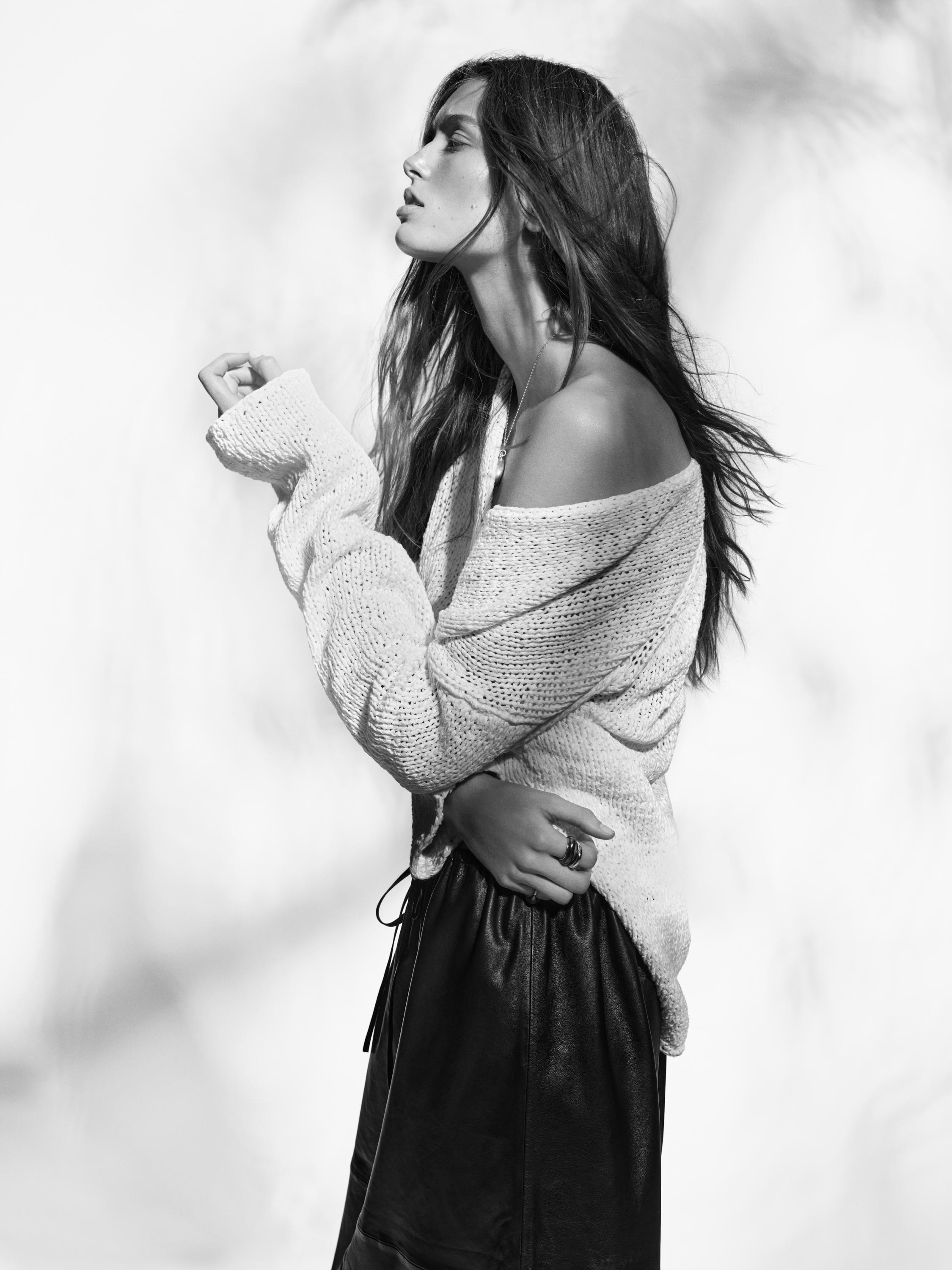 Πλάνο μέσο από πλεκτό λευκό πουλόβερ με έναν ώμο έξω και μαύρη φούστα.