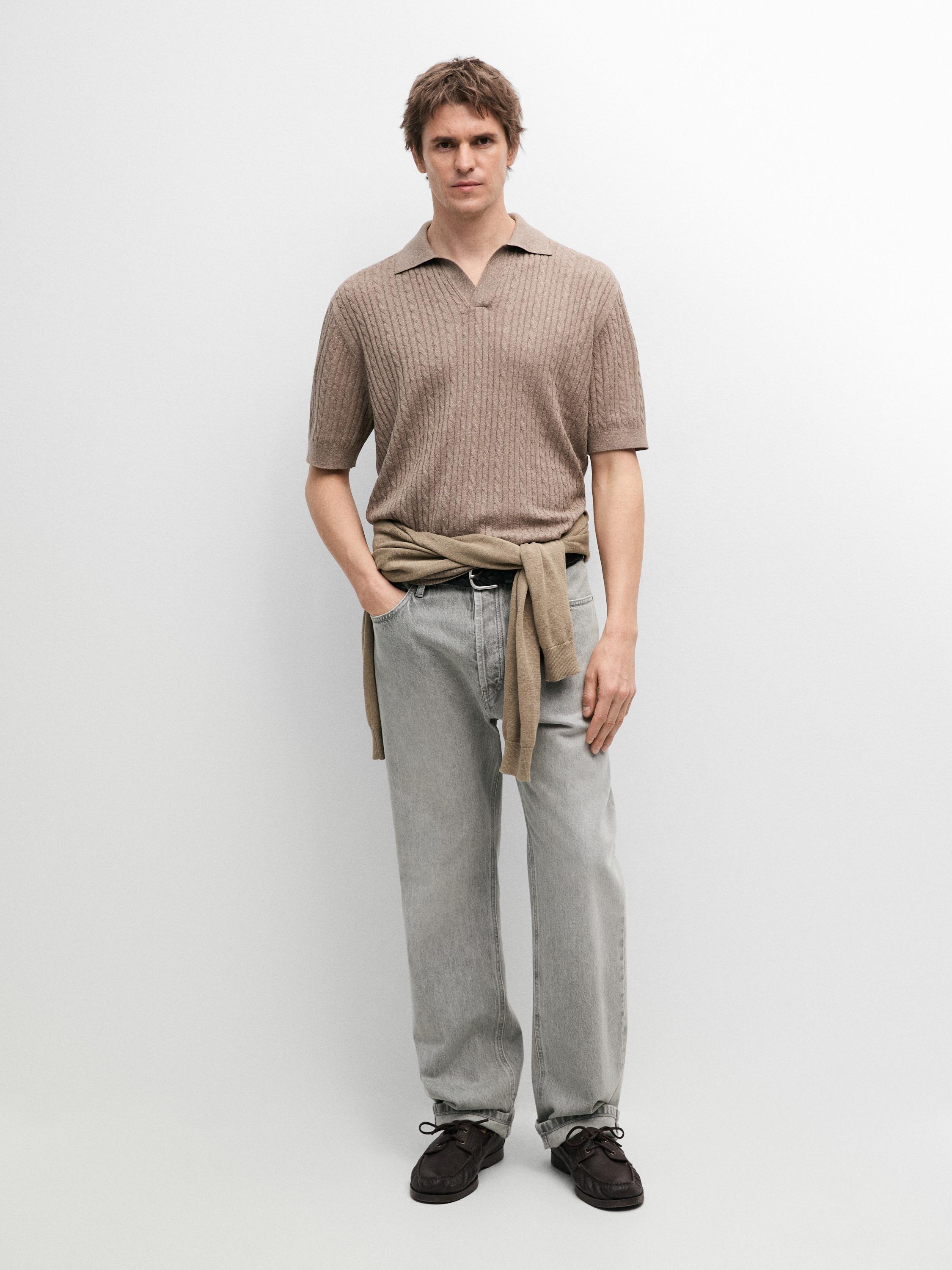 Conjunto de polo kaki claro con detalle trenzado, pantalones grises y zapatos oscuros. Suéter atado a la cintura.