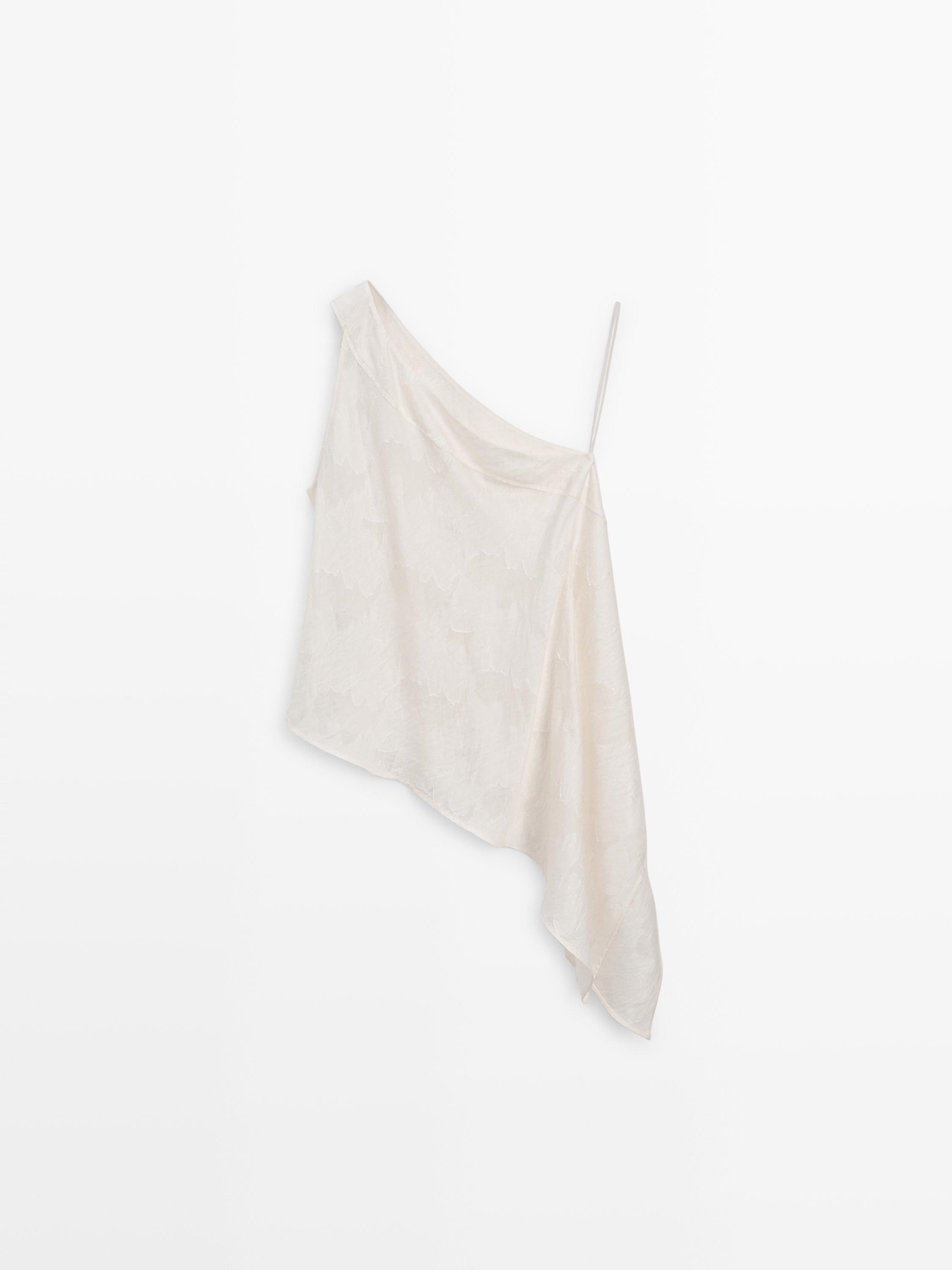 Vista frontal de top blanco con escote asimétrico y tirante fino en un lado. Diseño suelto y caída irregular.