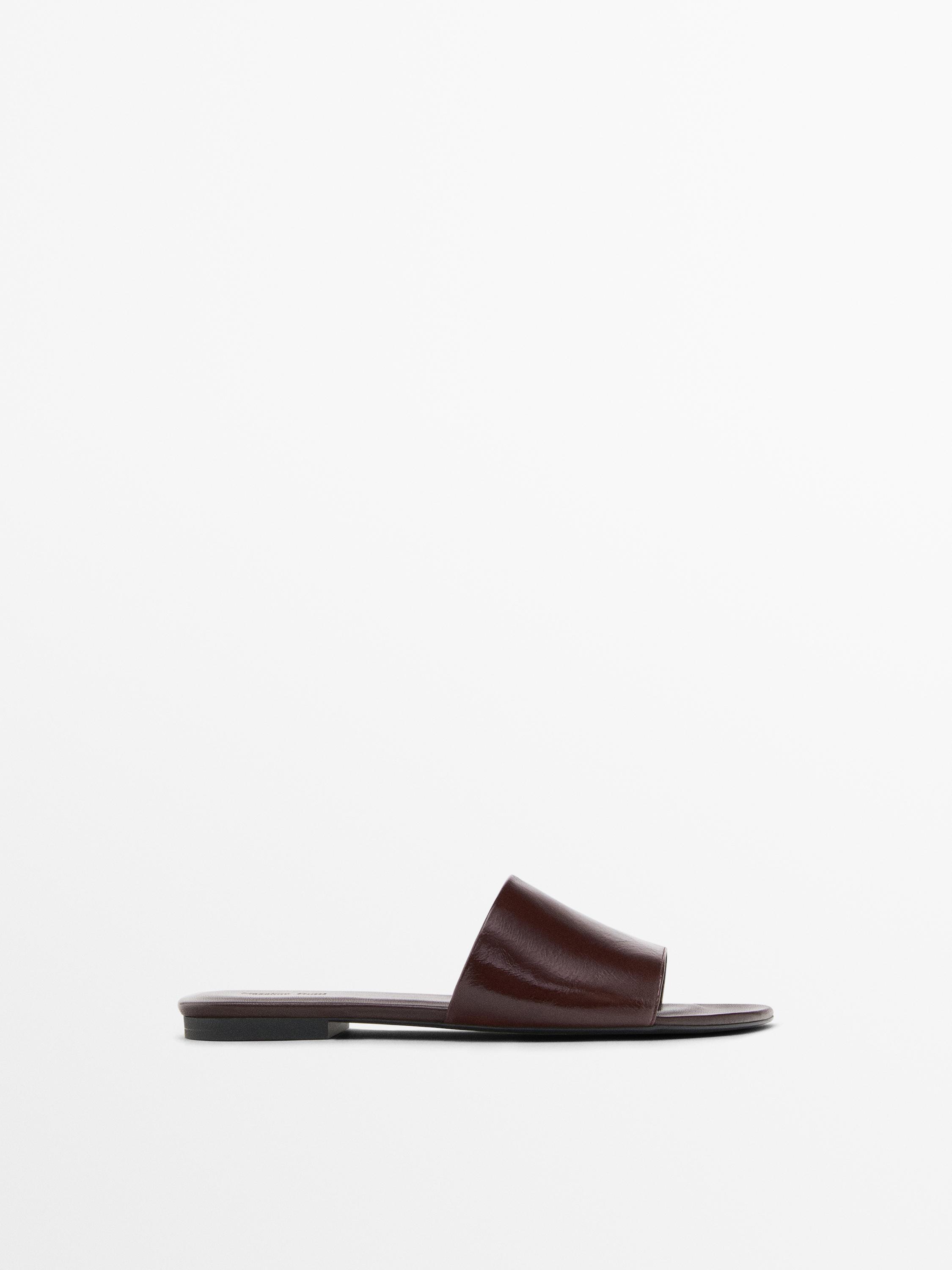 Side view of a dark brown flat sandal with a wide strap and thin sole.