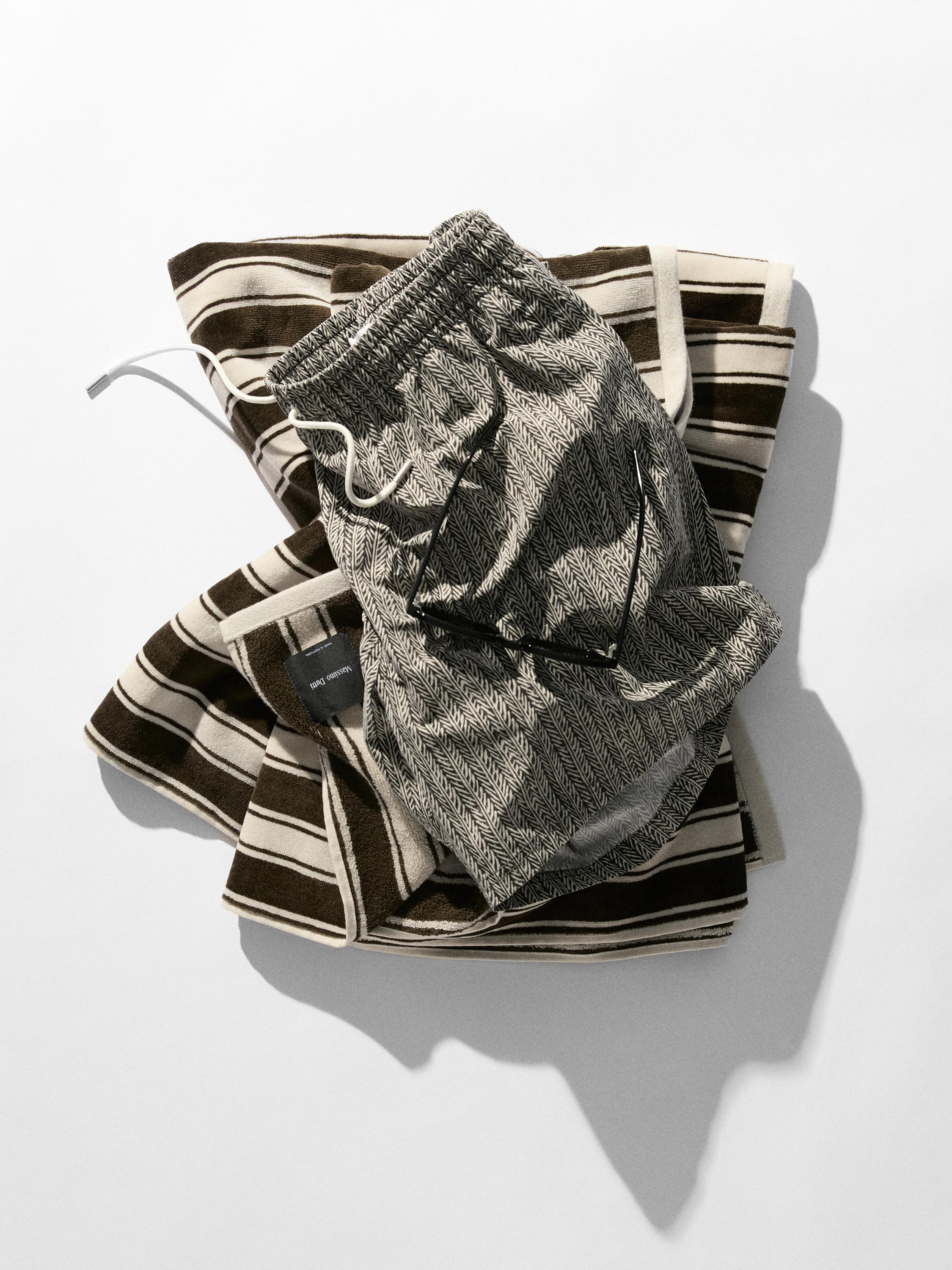 Vue de dessus d'un short à imprimé géométrique avec cordon de serrage blanc sur une serviette à rayures marron et blanches.