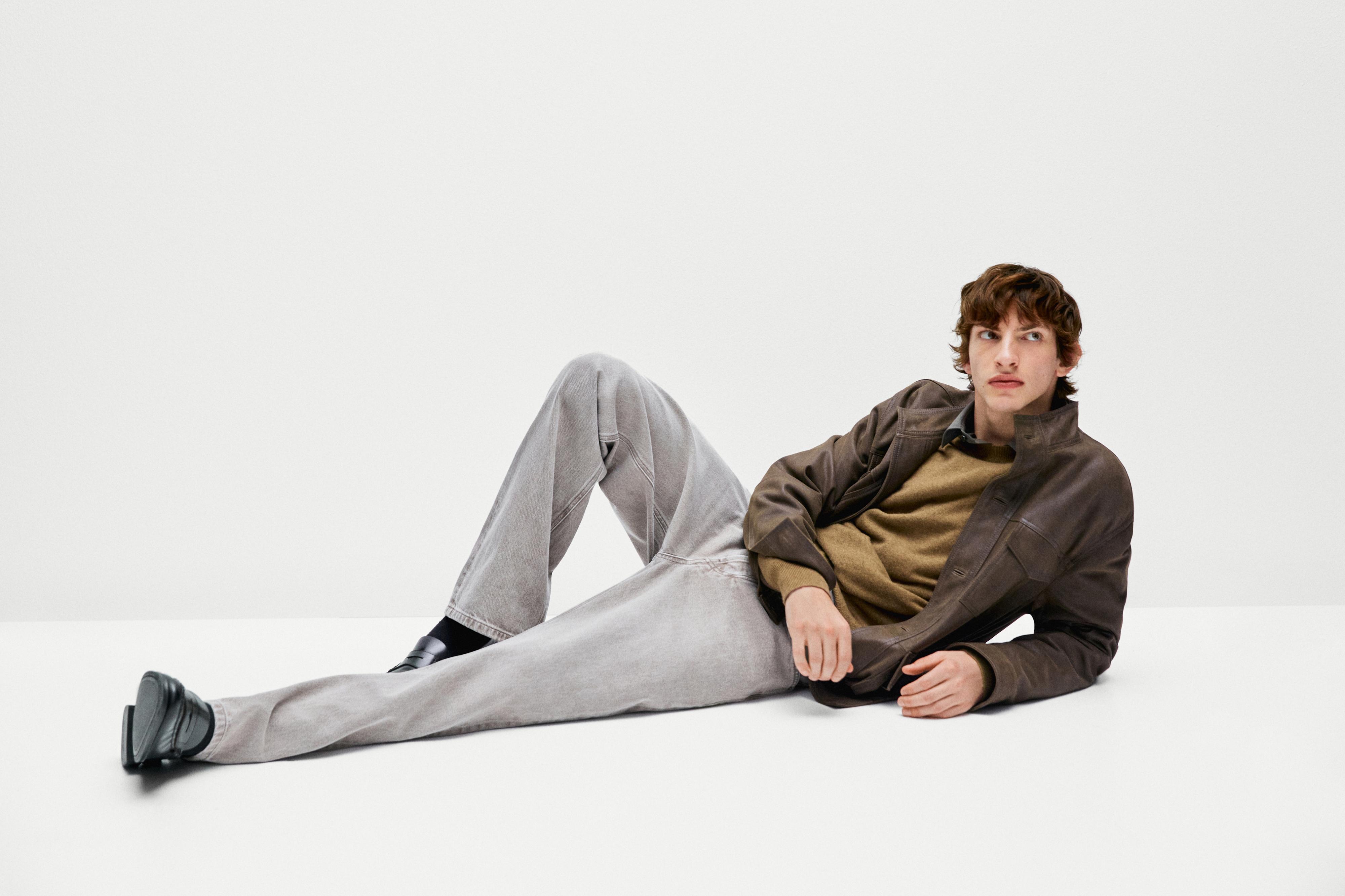 Set van bruine jas, beige trui, grijze broek en zwarte schoenen.