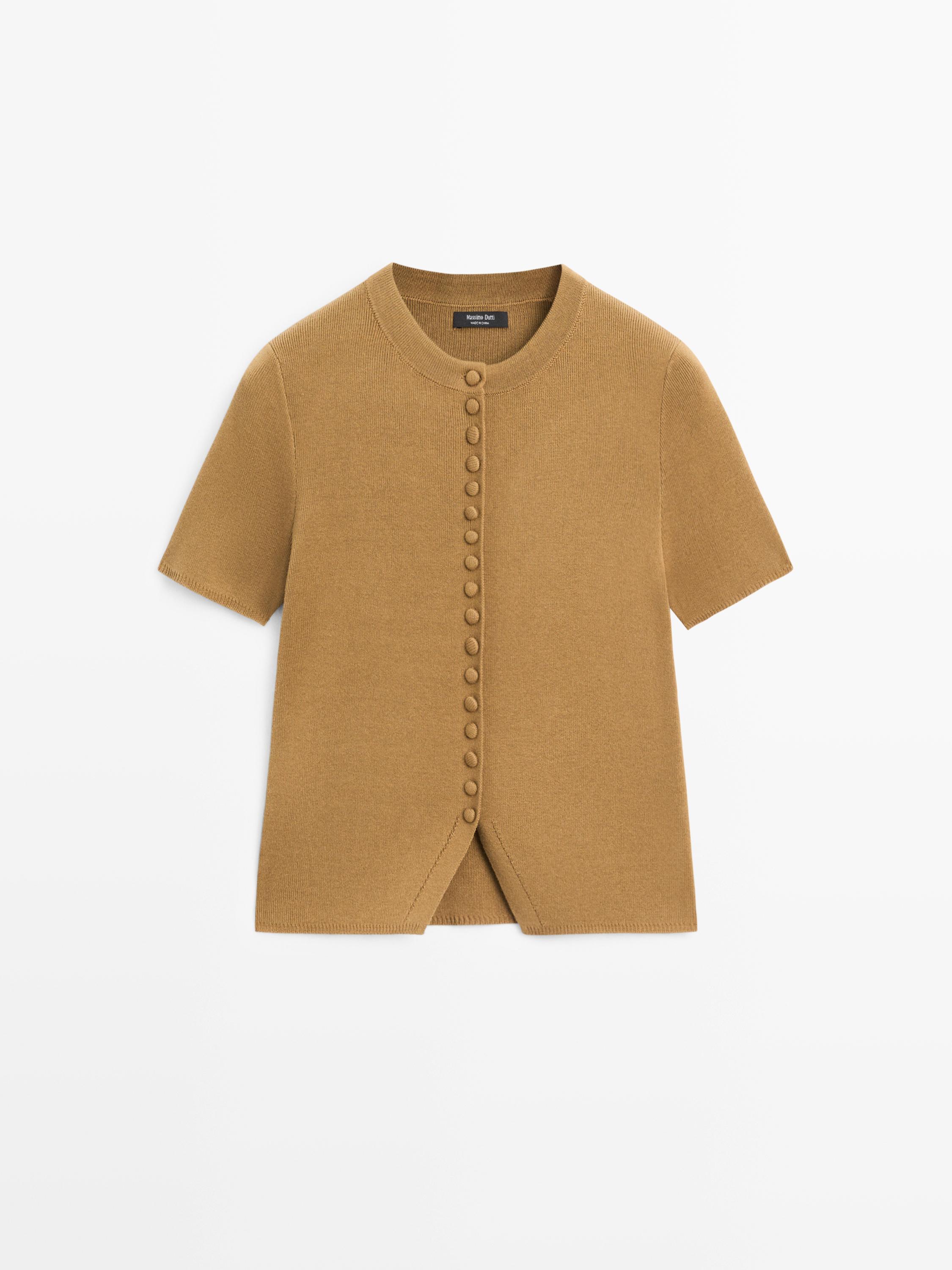 Vorderansicht einer vanillefarbenen Strickjacke, kurzärmelig, mit Knopfdetails vorne und Rundhalsausschnitt.