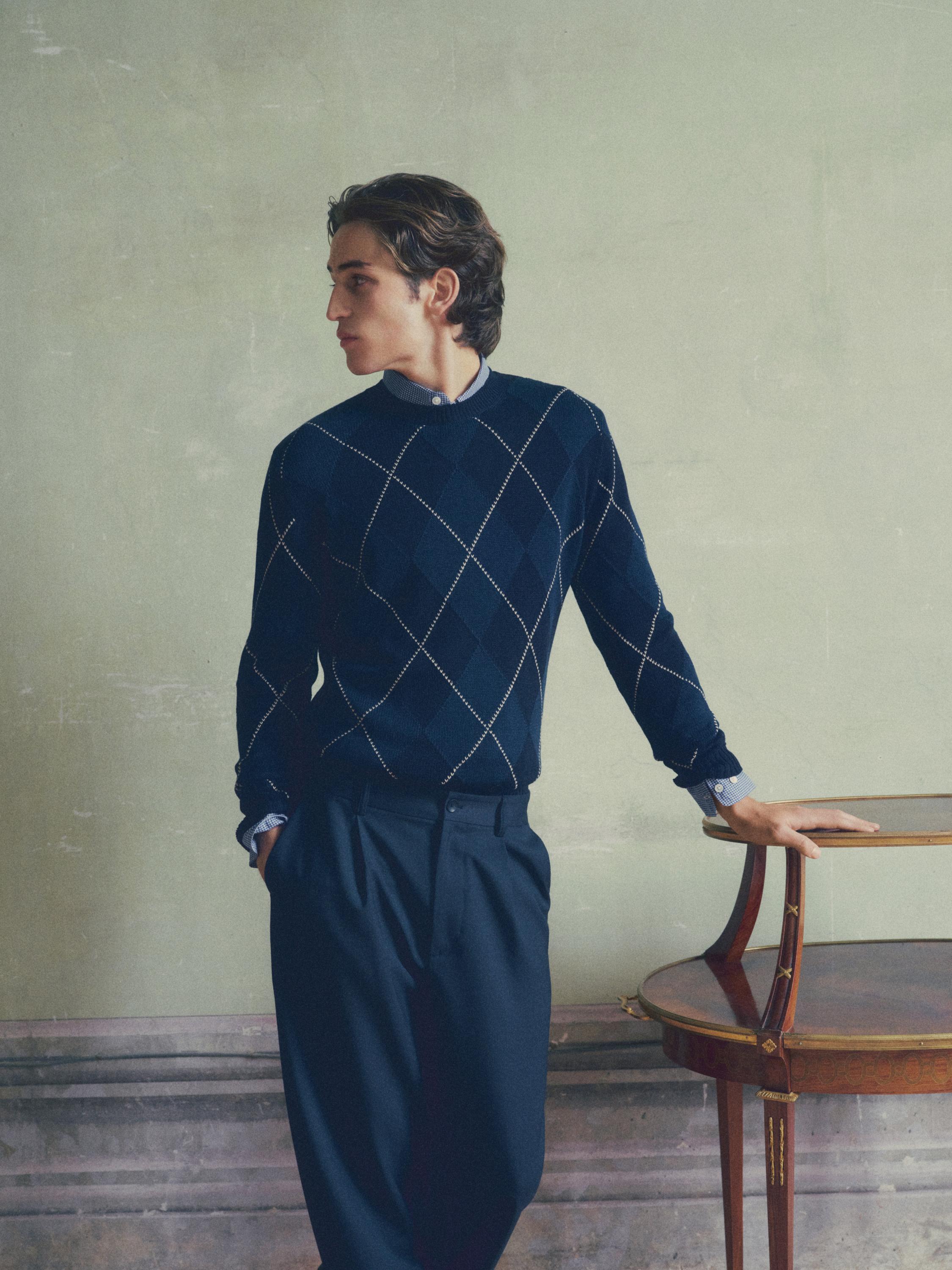 Conjunto de pantalón azul marino relaxed fit con pinzas y suéter azul con patrón de rombos.