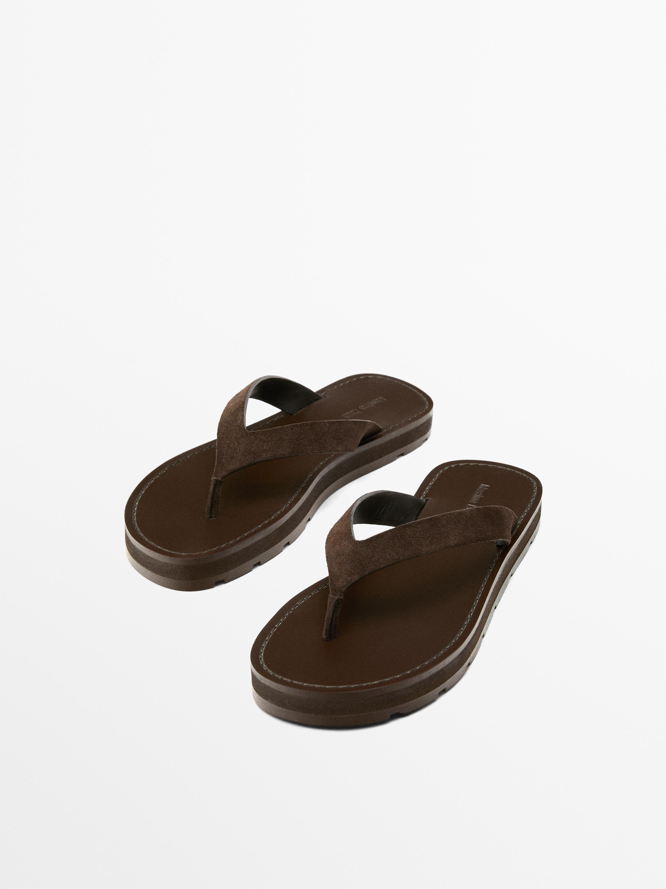 Vista frontal de sandalias planas marrones con tira en el dedo y suela gruesa.
