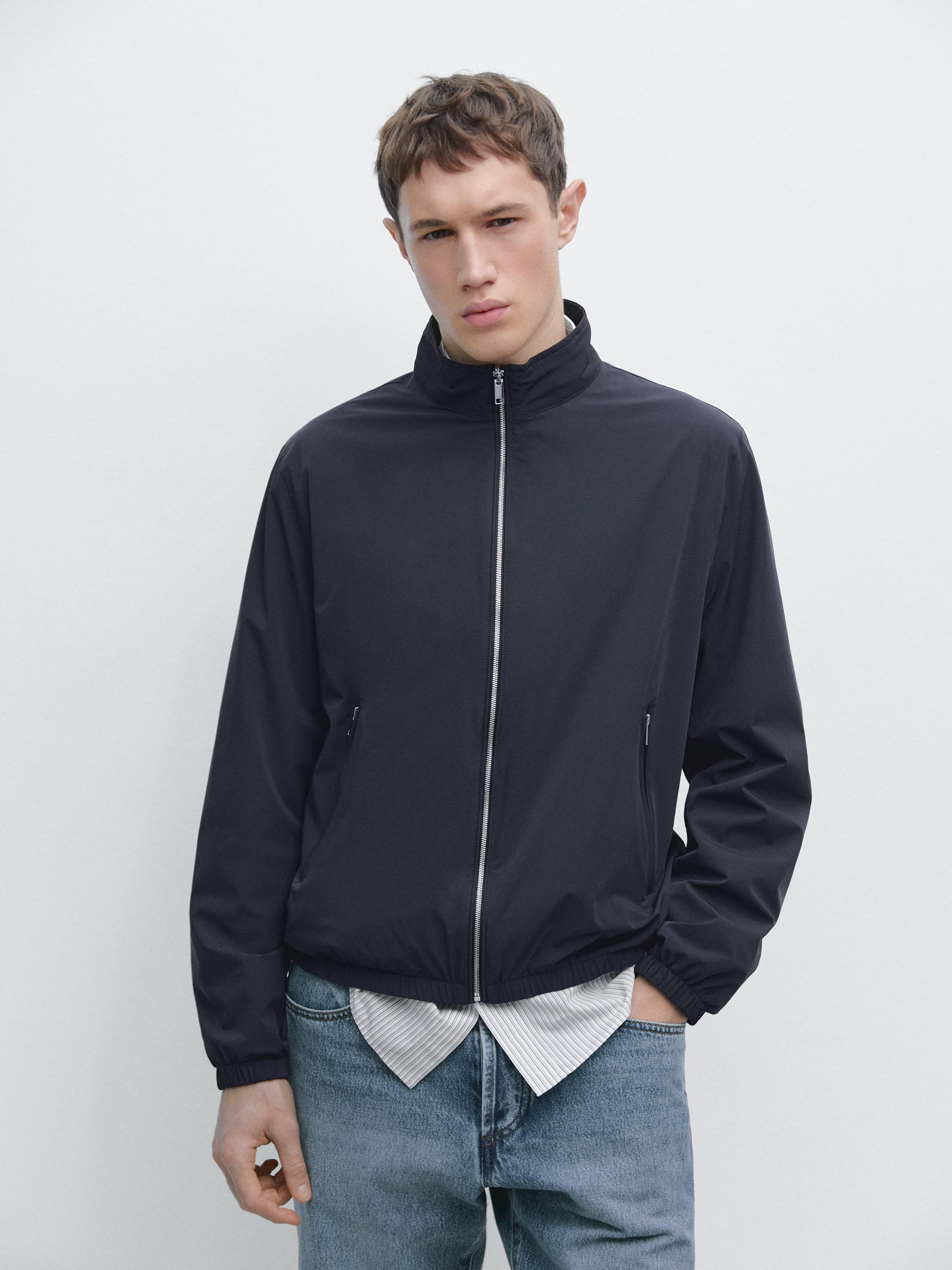 Merevärvi lukuga eest suletav ja küljetaskutega jakk, valge särgi ja siniste teksade peal.