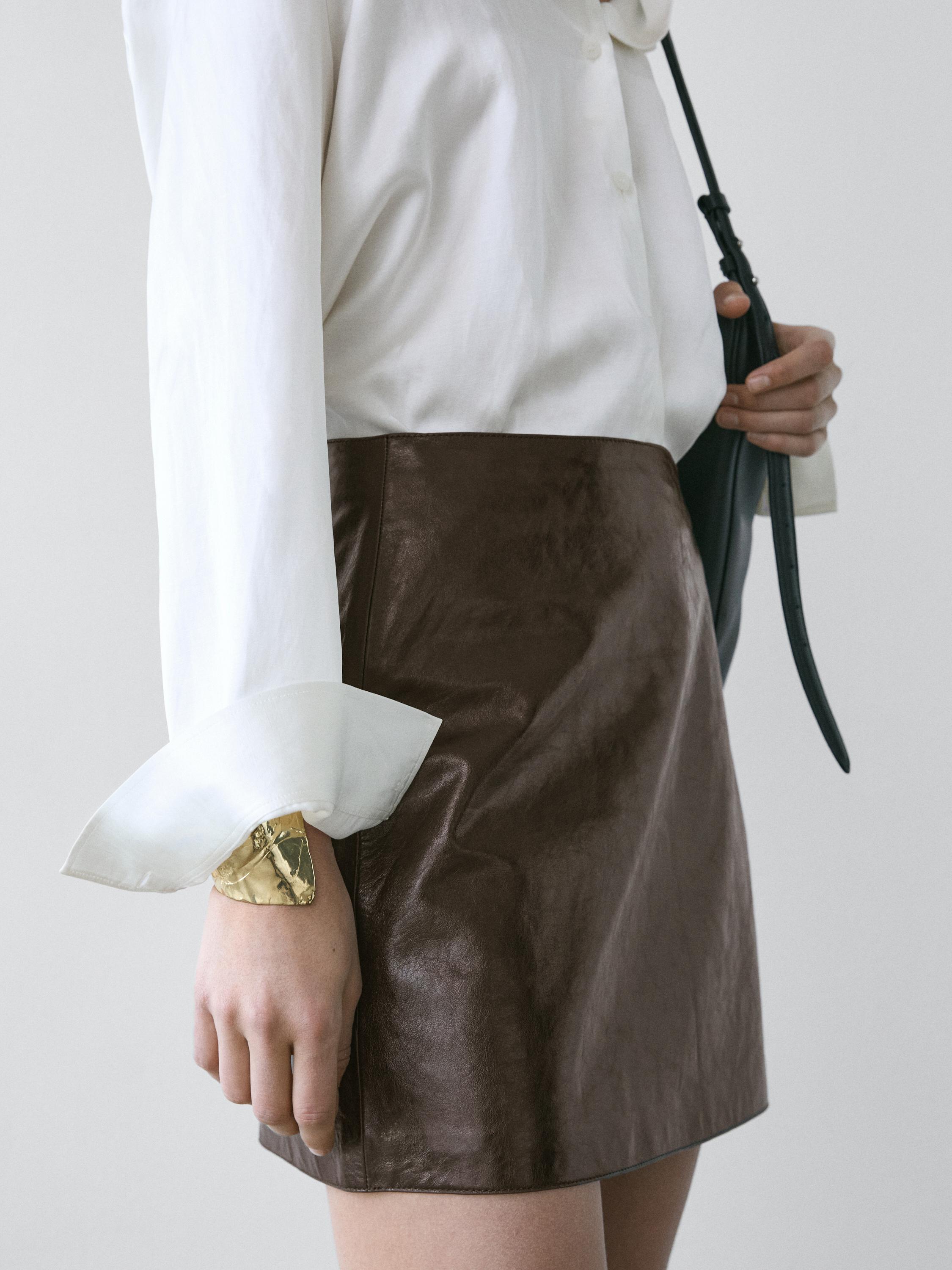 Medium shot of a brown mini skirt with a white long-sleeved blouse.