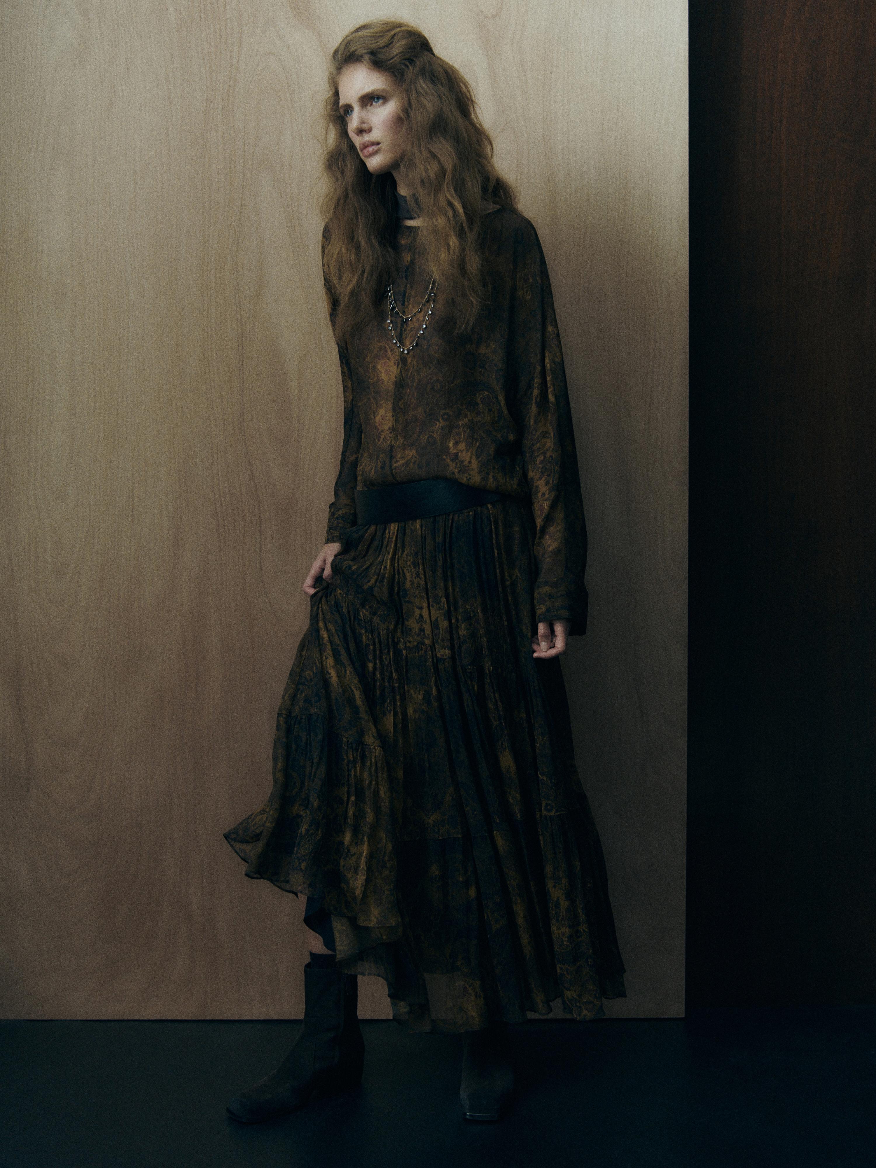 Ensemble blouse et jupe longue imprimées dans des tons foncés, avec des bottes noires.