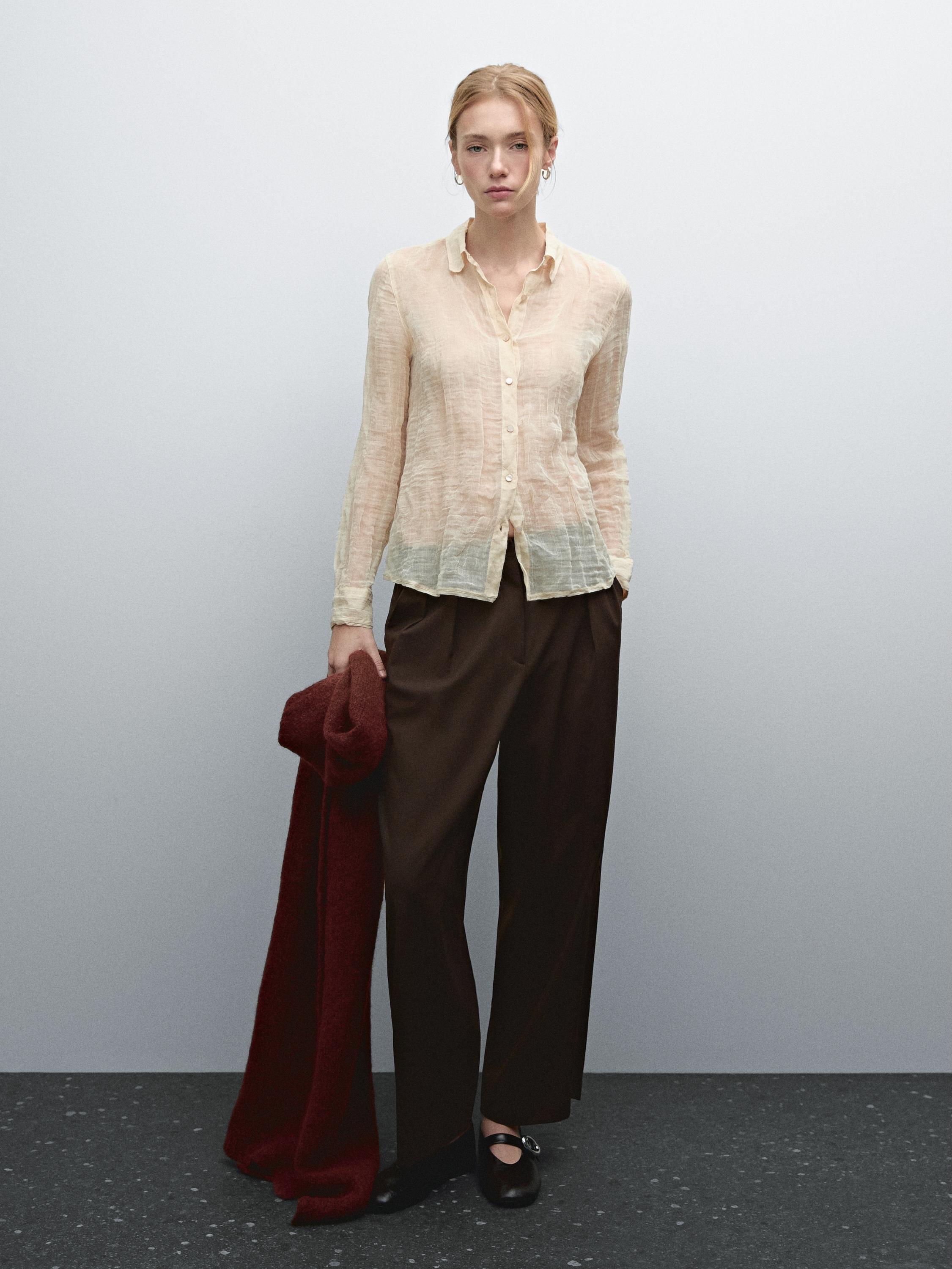 Conjunto de blusa beige transparente abotonada y pantalones marrones anchos con bufanda roja.