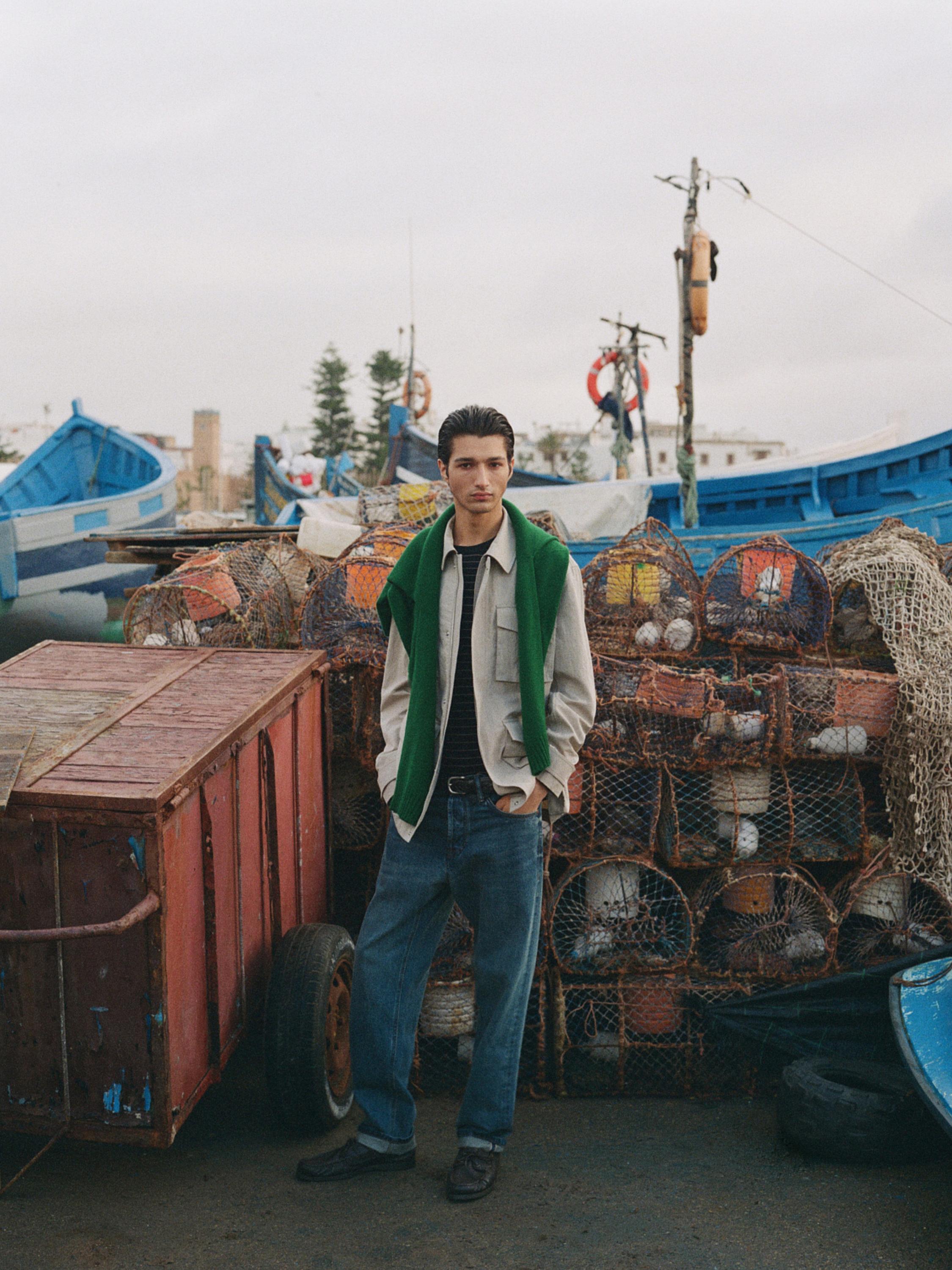 Conjunto de camisa beige, camiseta negra, jeans azules y suéter verde sobre los hombros.