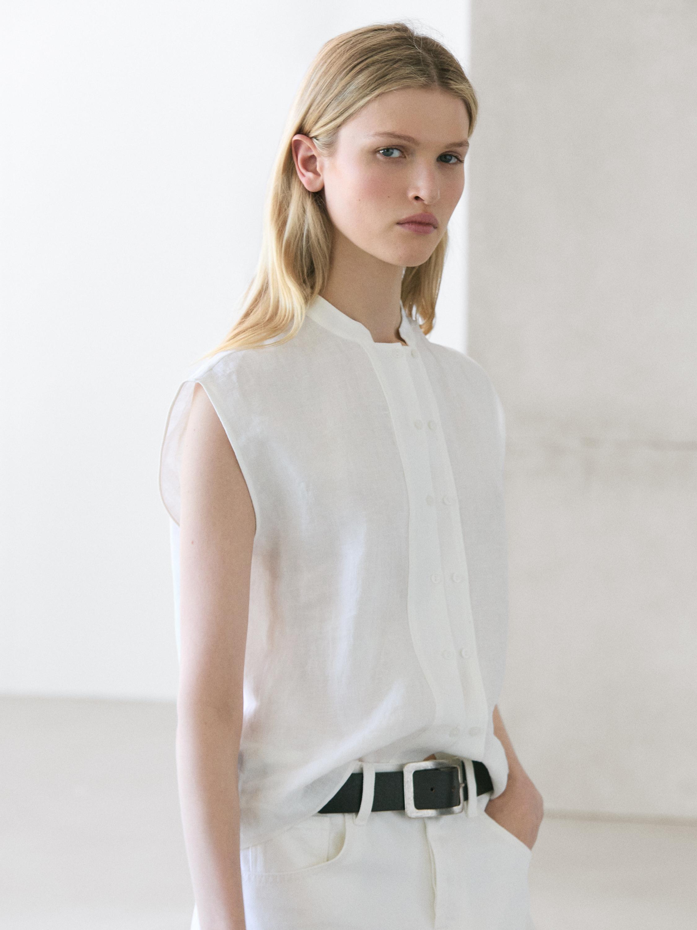 Plano medio de camisa blanca sin mangas con botonadura frontal y cuello mao.