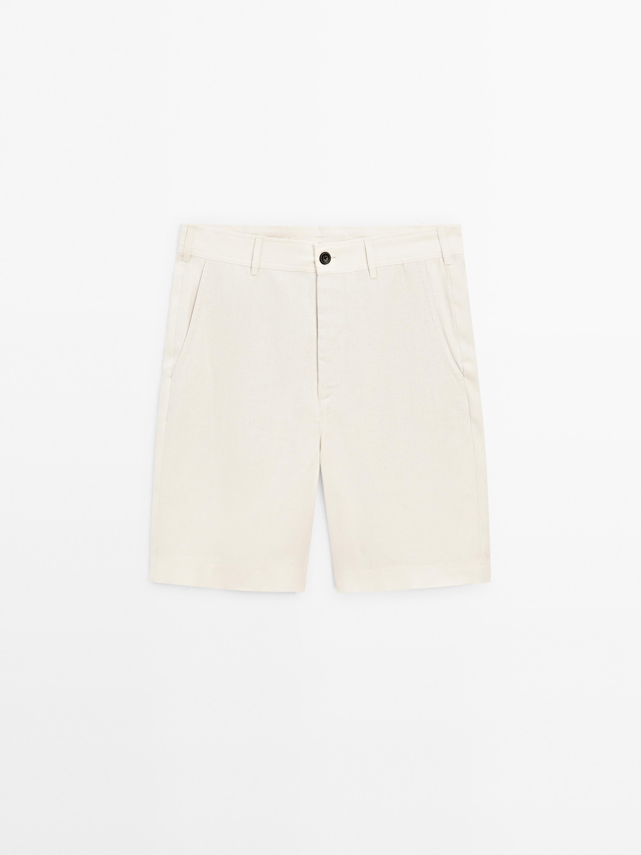 Tampilan depan celana pendek beige dengan saku samping dan kancing depan.