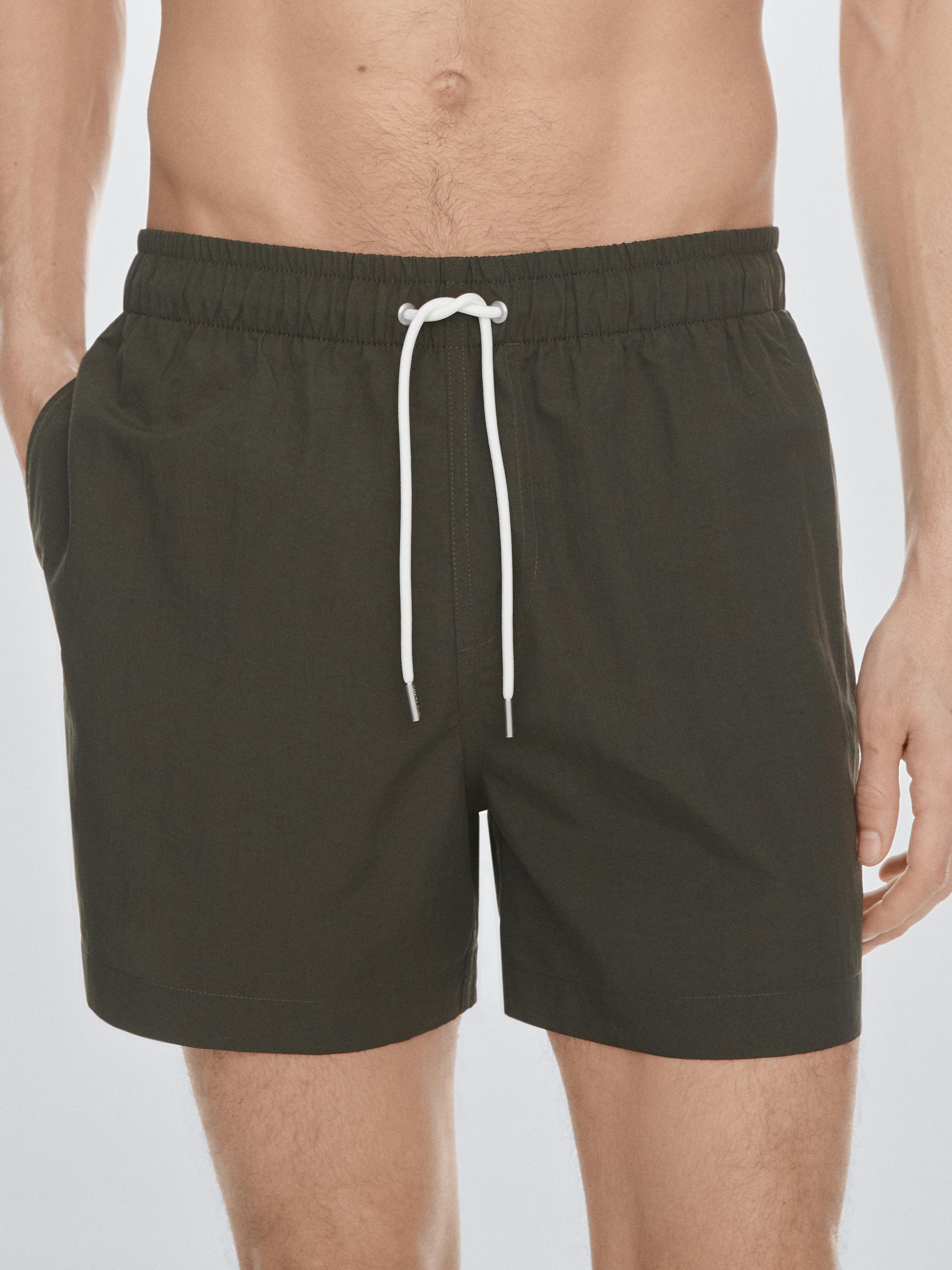 Halbaufnahme eines einfarbigen khakifarbenen Badeanzugs mit weißem Kordelzug und Seitentaschen.