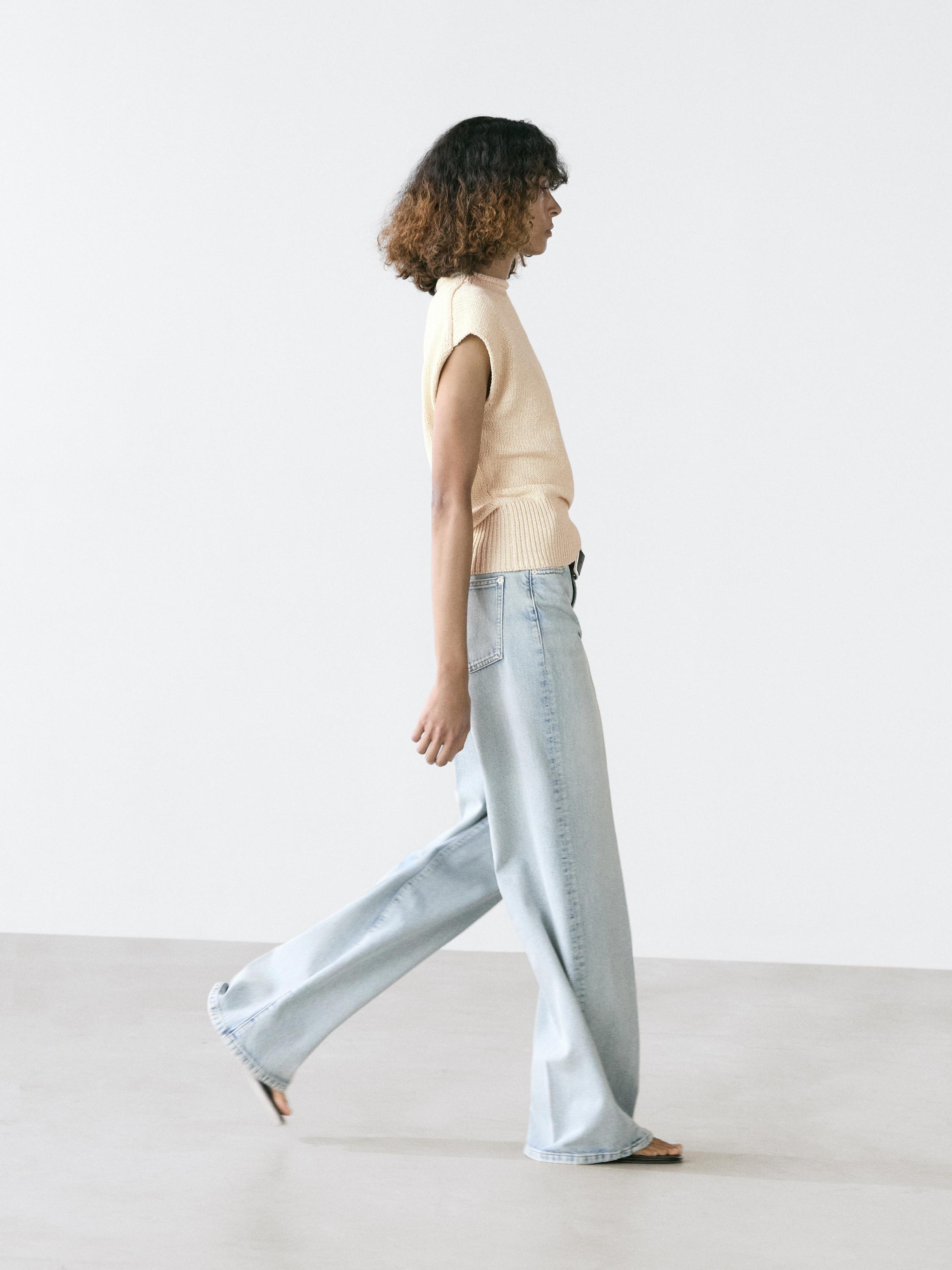 Set van mouwloze ecru gilet en lichtblauwe wijde jeans met achterzakken.