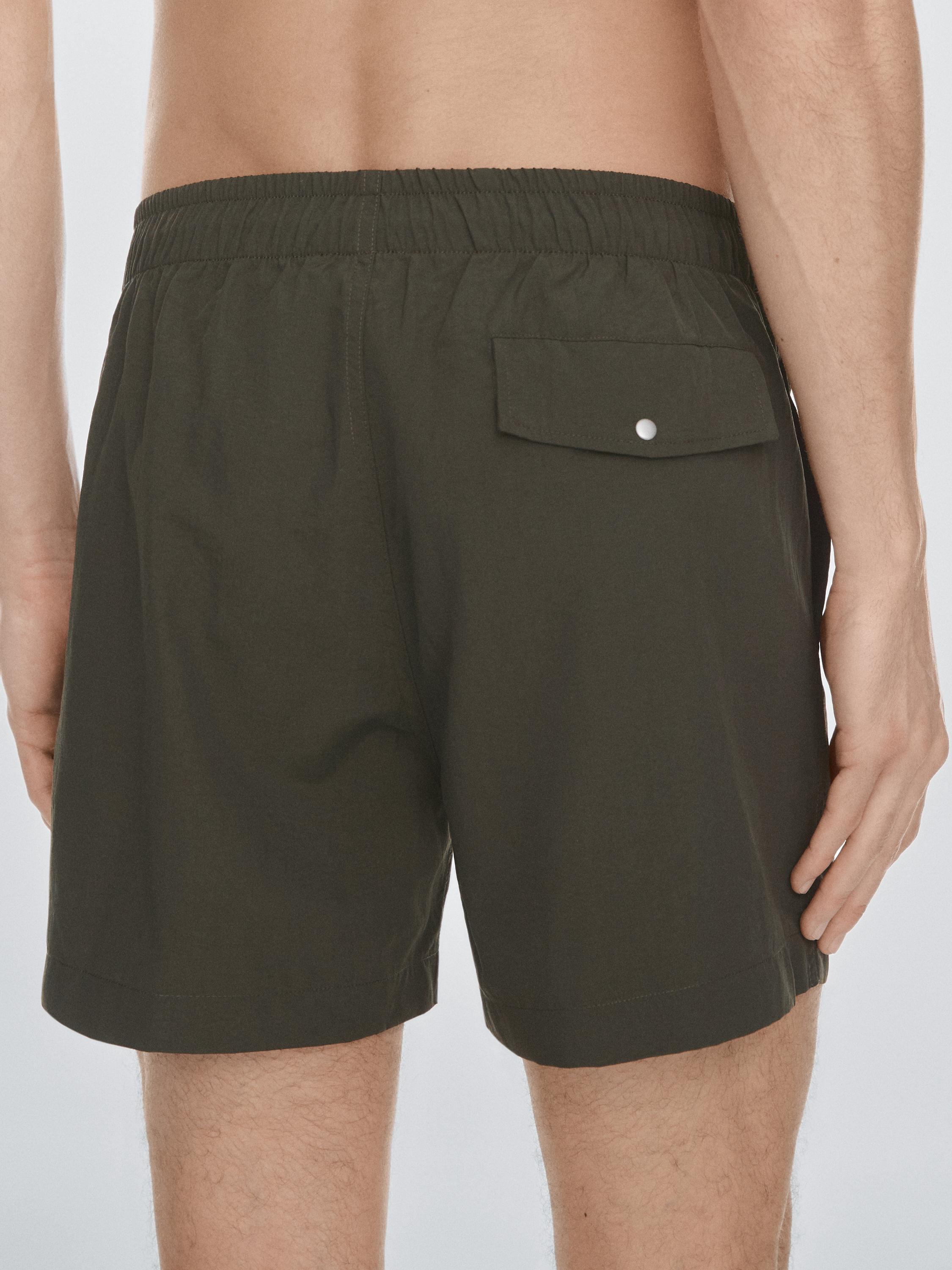 "Halbnahe Einstellung einer khakifarbenen Badehose mit elastischem Bund und Gesäßtasche mit Patte und Knopf."