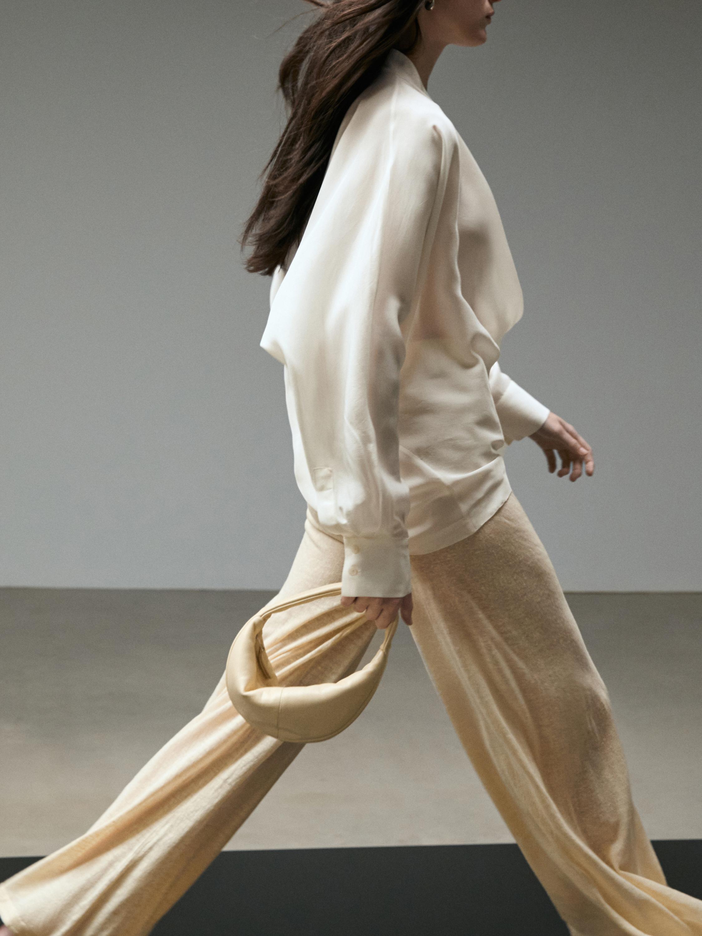 Conxunto de blusa branca de manga longa e pantalóns suaves vainilla, con bolso de man beixe.