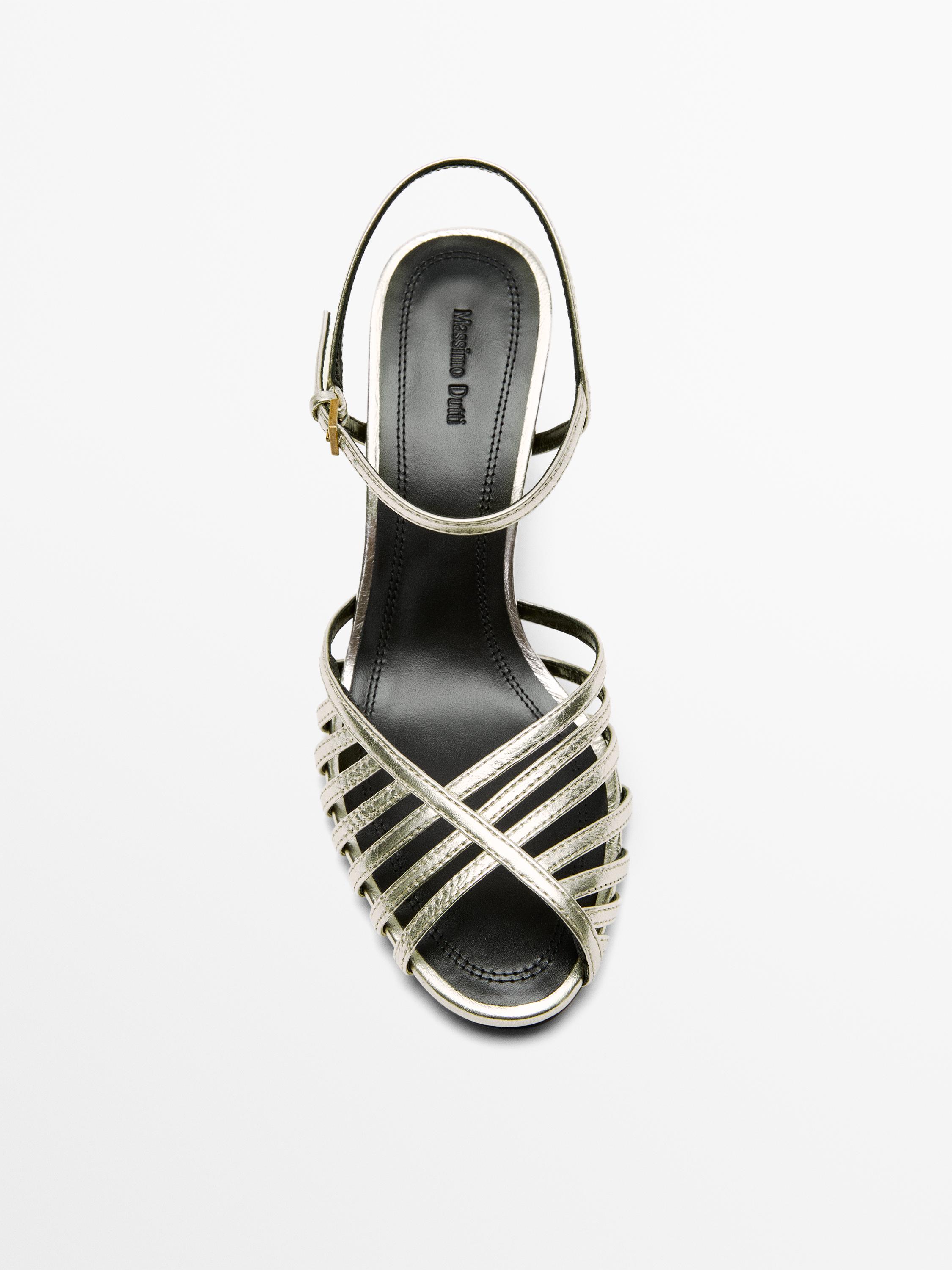 منظر علوي لصندل بكعب بلون البلاتين مع أحزمة متقاطعة وإبزيم جانبي. نص ظاهر: "Massimo Dutti".